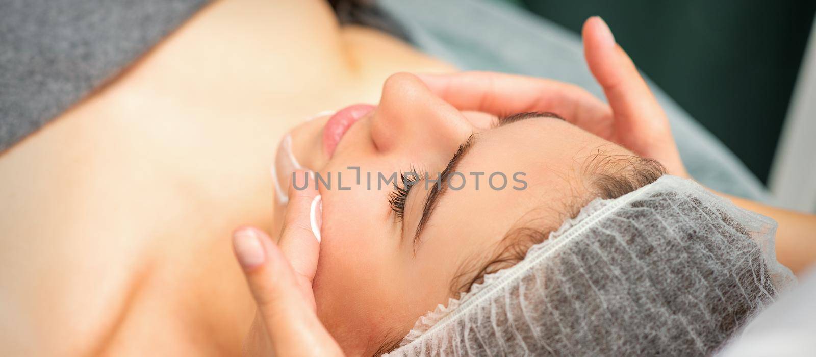 Spa facial skincare. Close-up of a young caucasian woman getting spa moisturizing face massage treatment at beauty spa salon