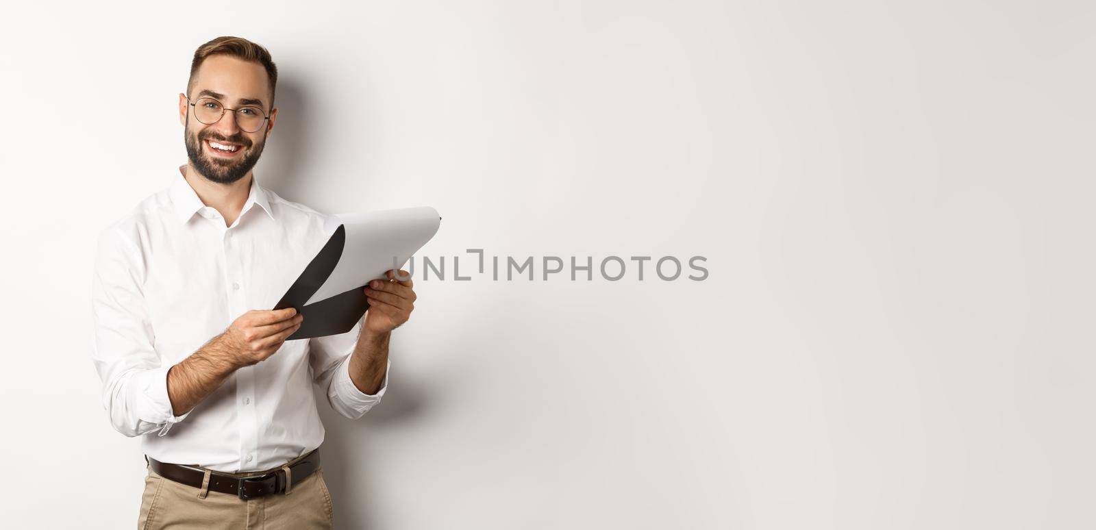 Employer looking satisfied at CV, reading document and smiling, standing over white background.