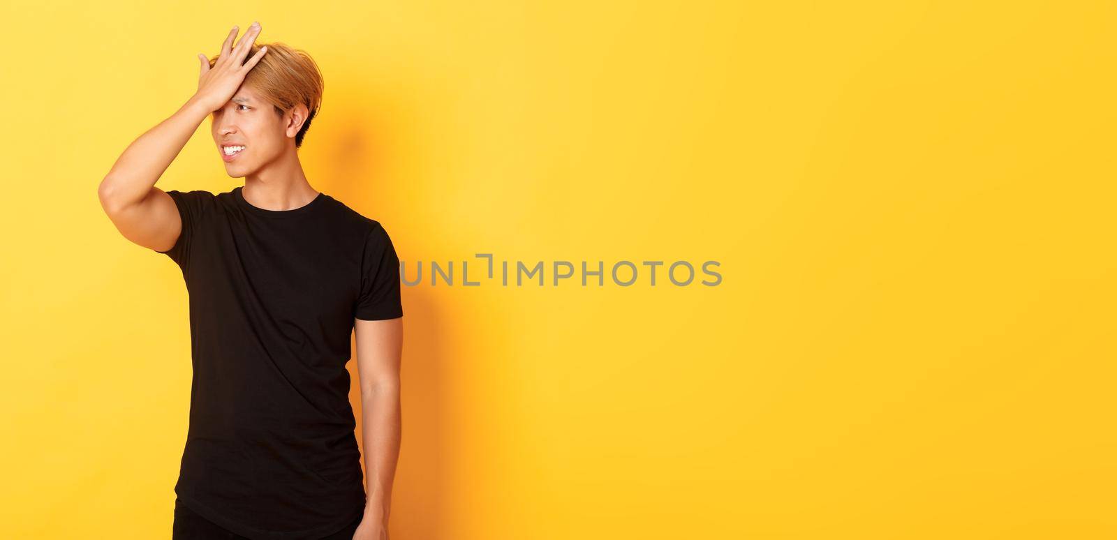 Upset and troubled asian guy snap forehead forgetful, standing over yellow background.