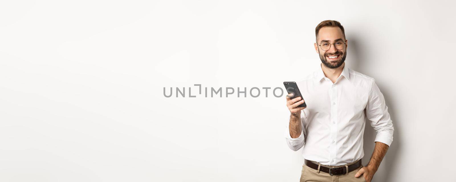 Handsome manager using smartphone and smiling pleased, sending text message, standing over white background.