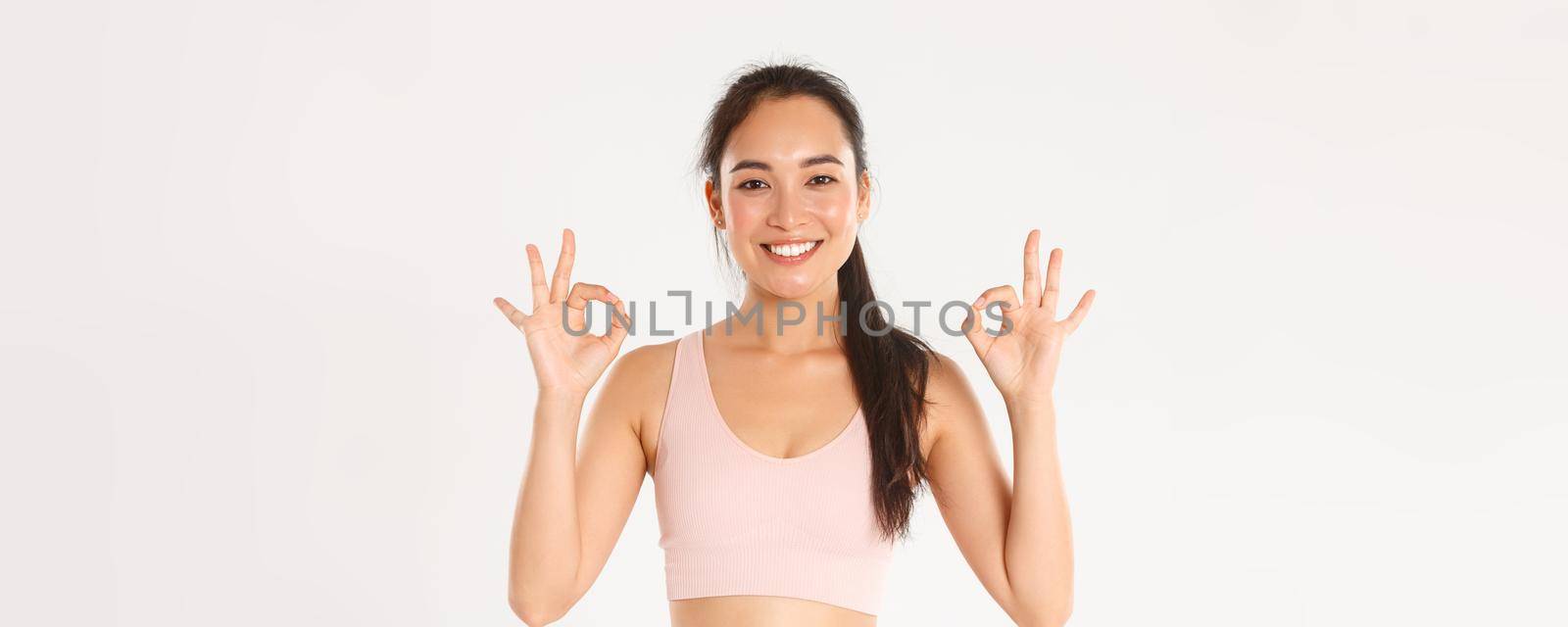 Sport, wellbeing and active lifestyle concept. Close-up of smiling, satisfied asian sportswoman recommend gym or yoga classes, showing okay gesture, pleased with perfect online coach by Benzoix