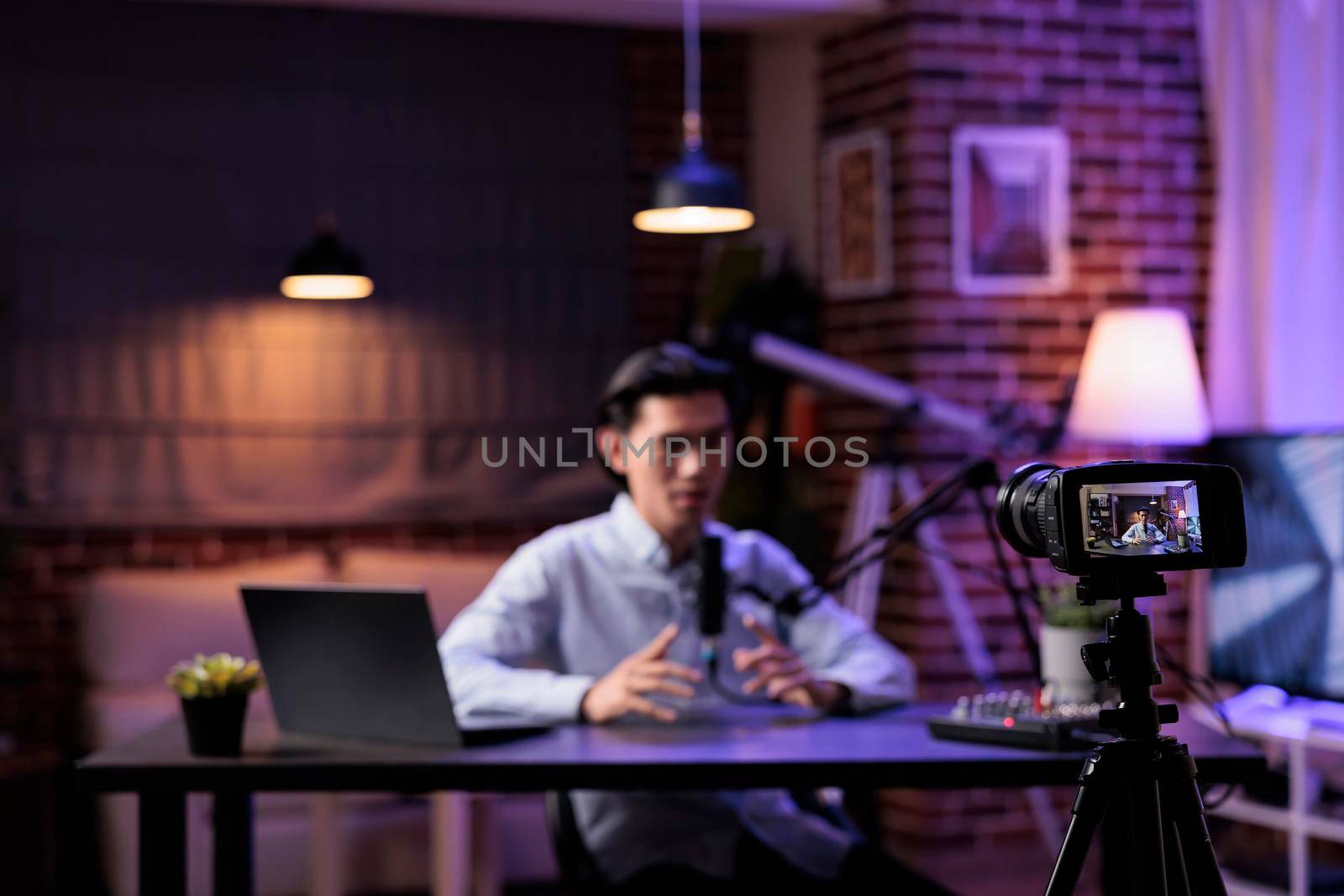 Content creator broadcasting talk show on camera, recording podcast episode with audio equipment. Filming video for internet channel, livestreaming social media vlog at sound station with laptop.