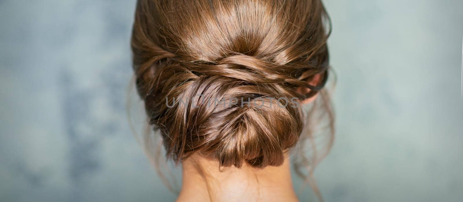 Rearview of young brunette woman with beautiful middle bun hairstyle on gray background