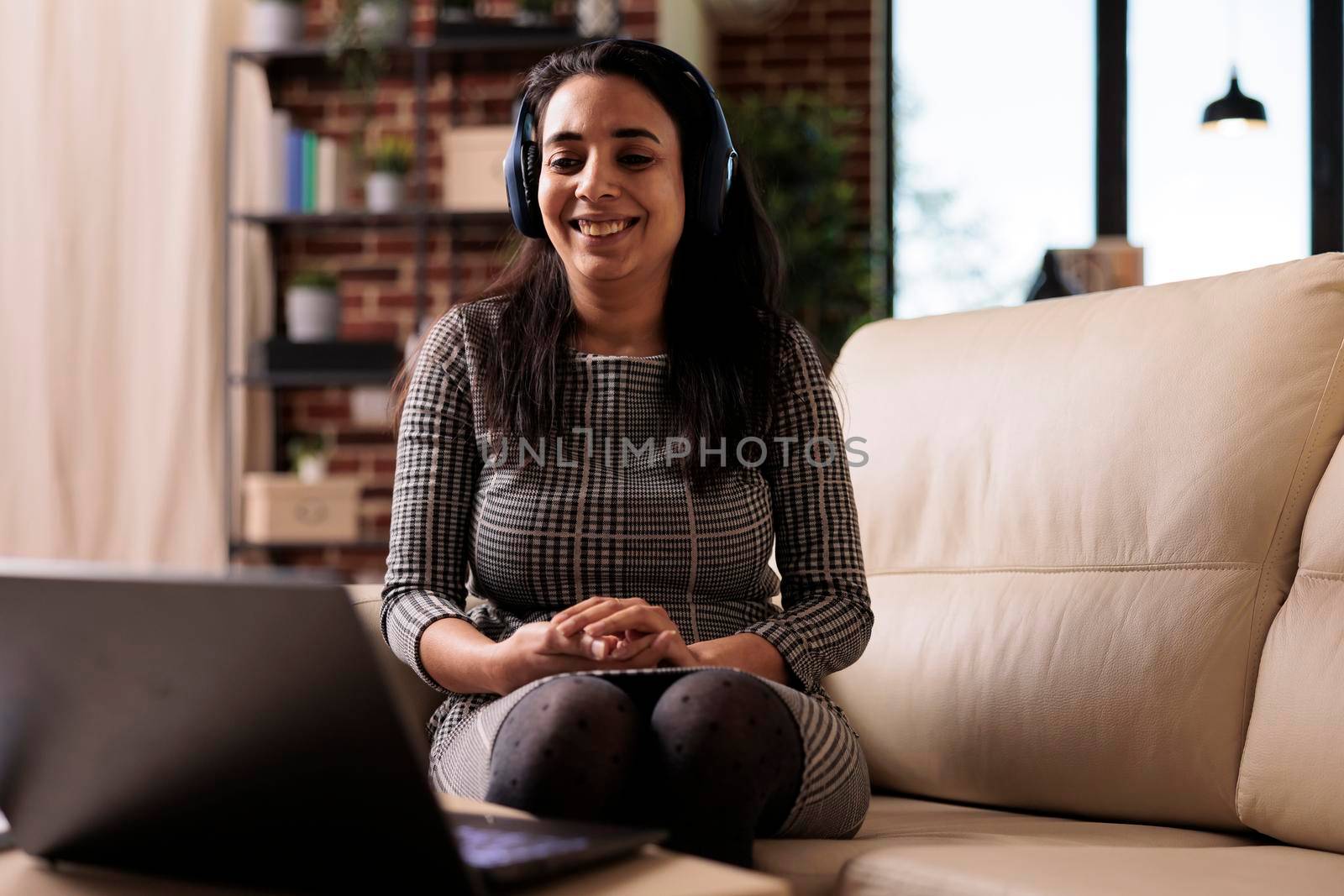 Freelancer working on laptop with headphones and listening to music or podcast. Attending online webinar lesson or enjoying song while she does remote business work on computer at home.