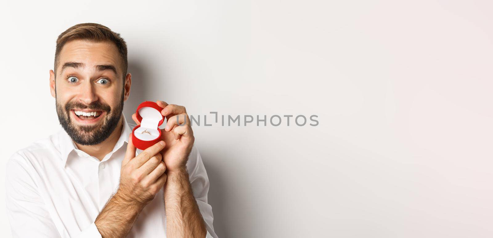 Close-up of handsome guy making proposal, looking hopeful and showing wedding ring, asking marry him, white background.