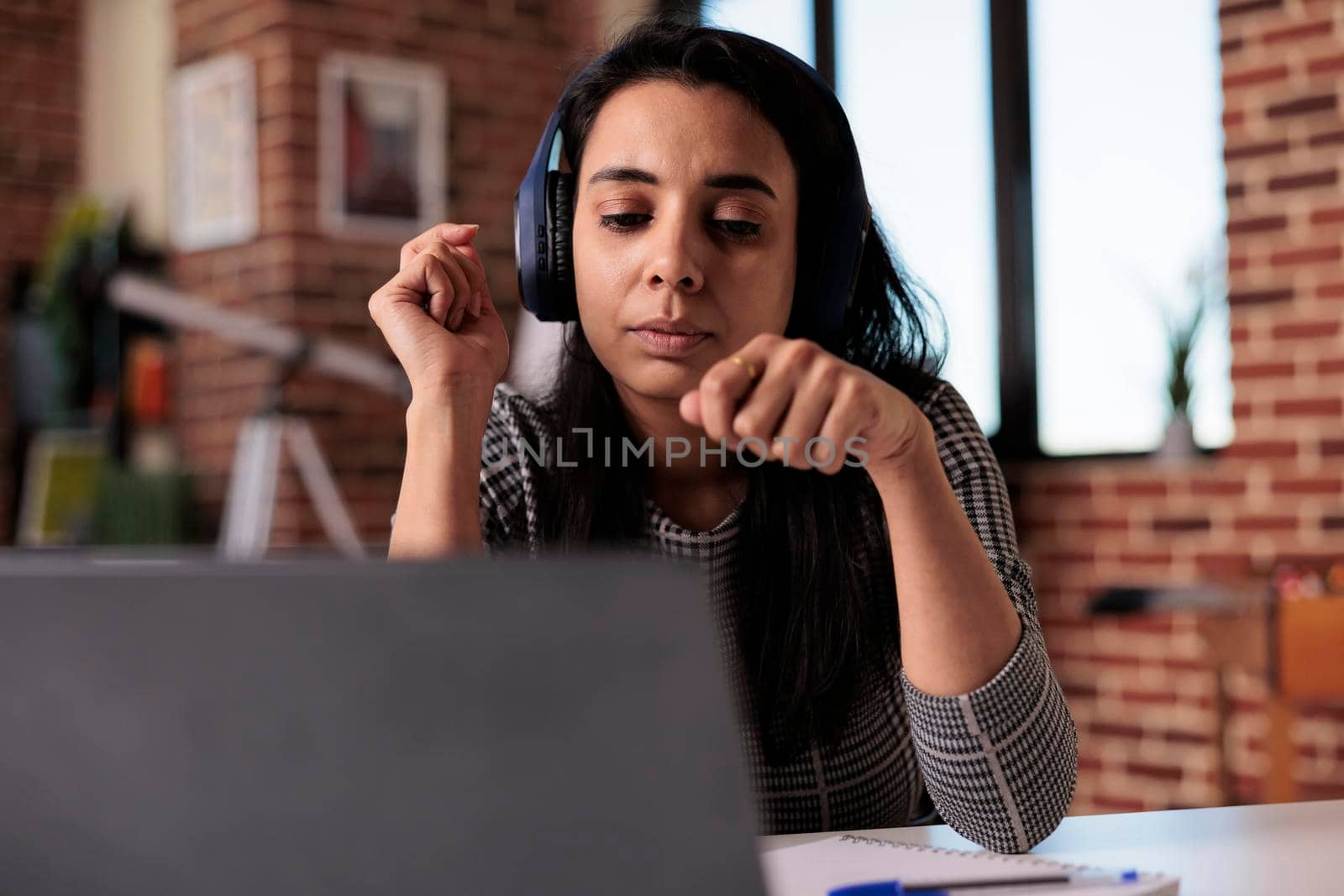 Young freelancer working on laptop with headphones, listening to music or online podcast at remote job. Attending webinar lesson or enjoying song while using computer at home office.