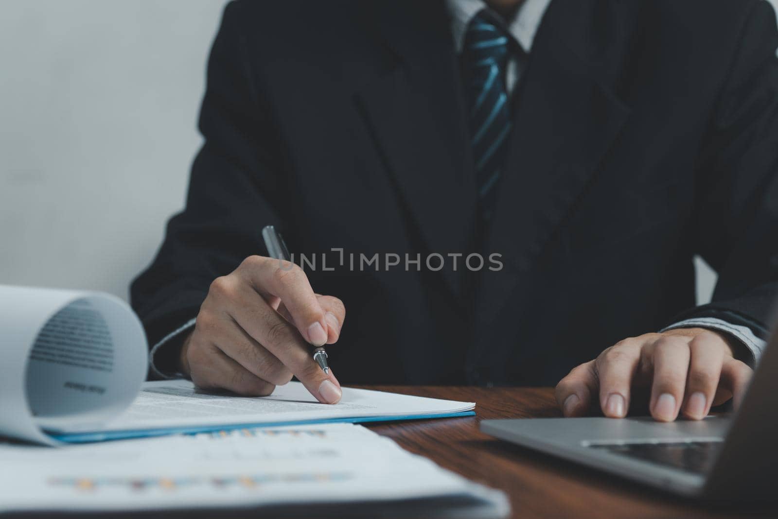 Businessman holding pen document graph accounting finance paper work analysis chart marketing investment and report economy with computer laptop on desk at office. by aoo3771