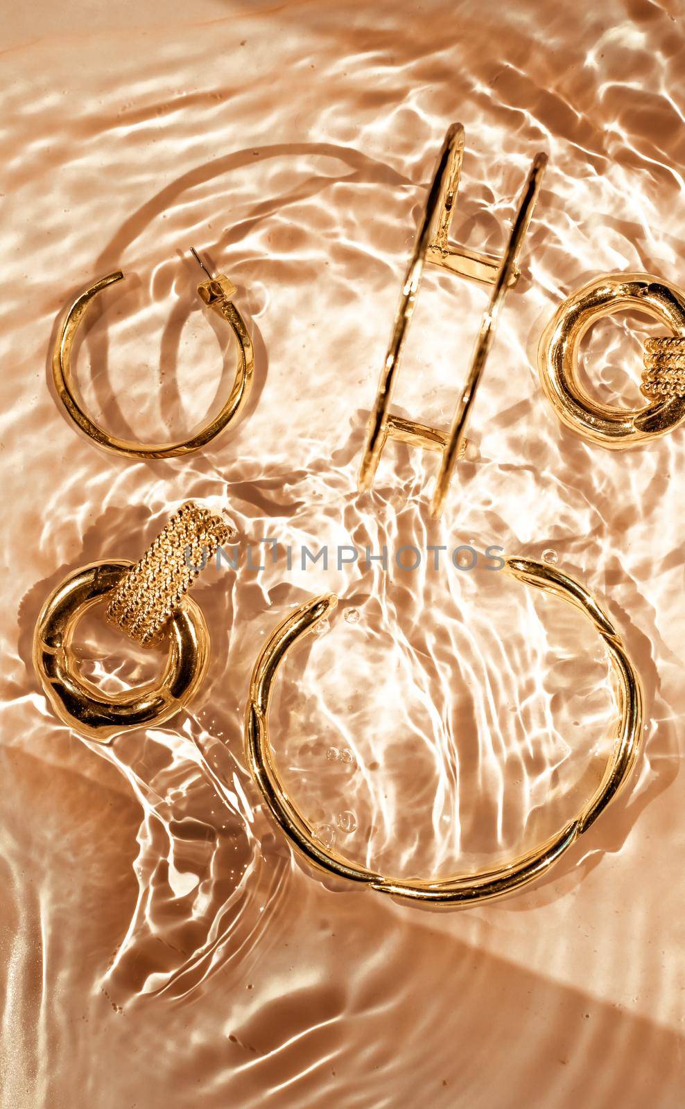 Golden bracelets, earrings, rings, jewelery on gold water background, luxury glamour and holiday beauty design for jewelry brand ads by Anneleven