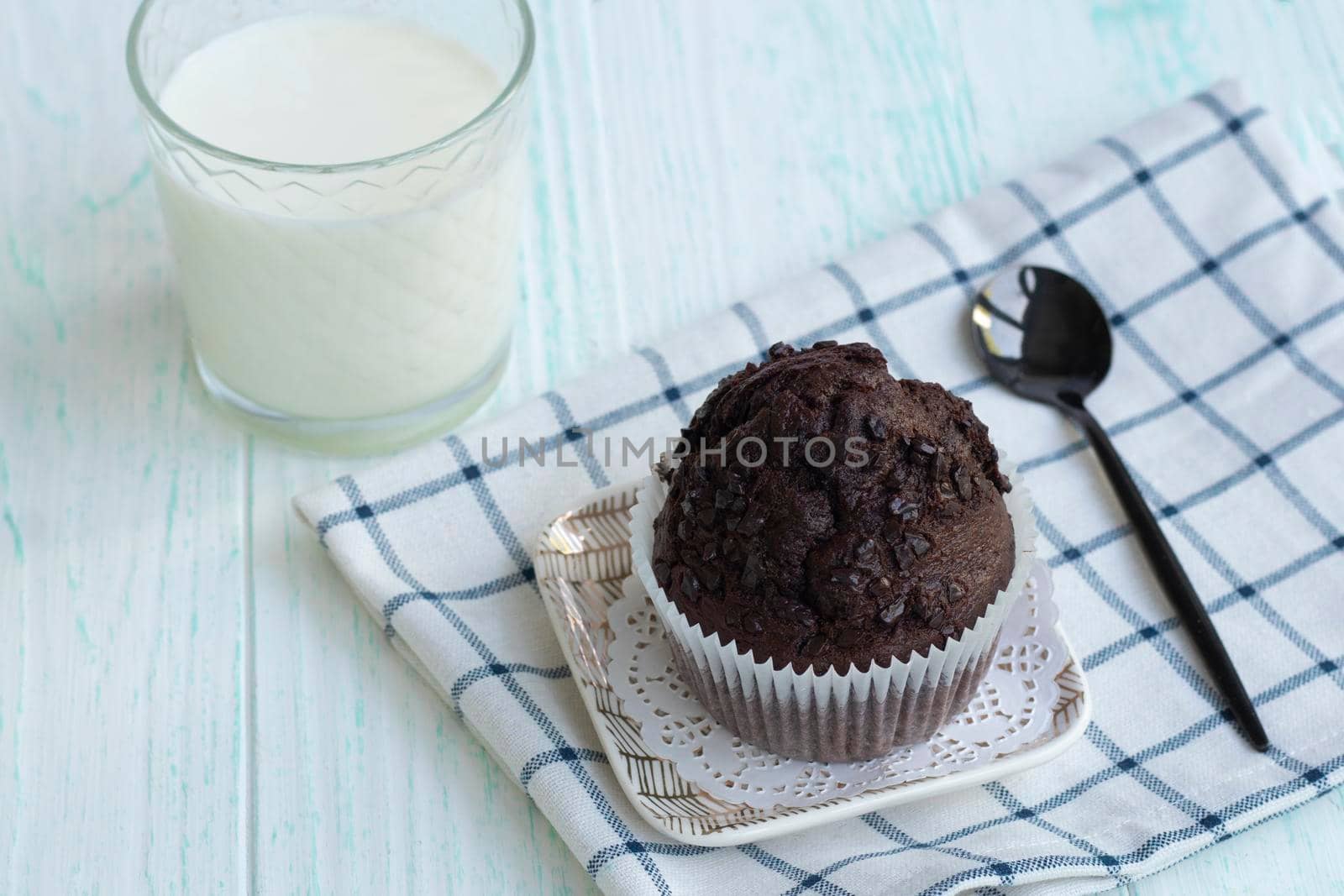 cupcake with chocolate chips stands on a napkin on a light wooden background. chocolate muffin with a glass of milk and a spoon. A beautiful breakfast with homemade pastries