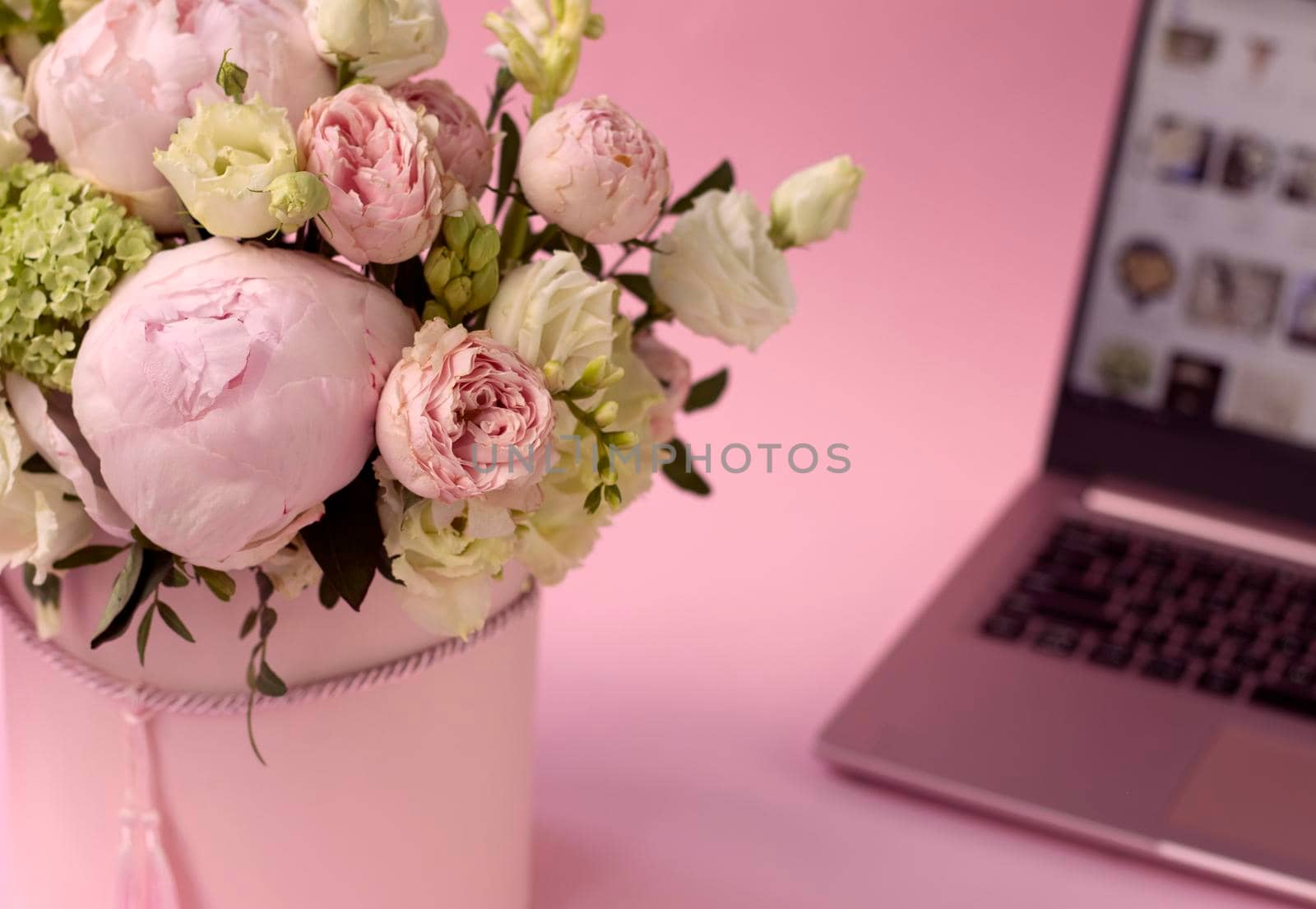 bouquet of flowers in a box close-up, against the background of an open laptop. Selective focus. Hydrangea, roses and peonies on a pink background. home delivery concept, buying flowers online.