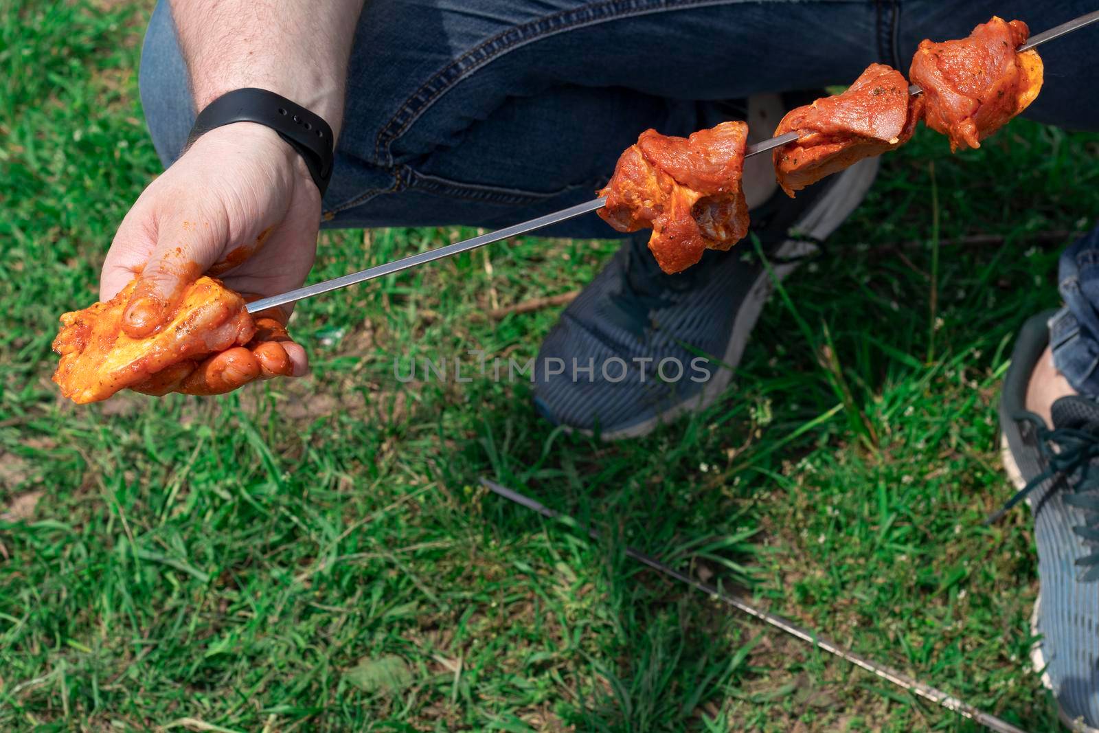 The cook in the open air Man preparing a shish kebab, close-up. Male hand puts the meat on the skewer outside. High quality photo