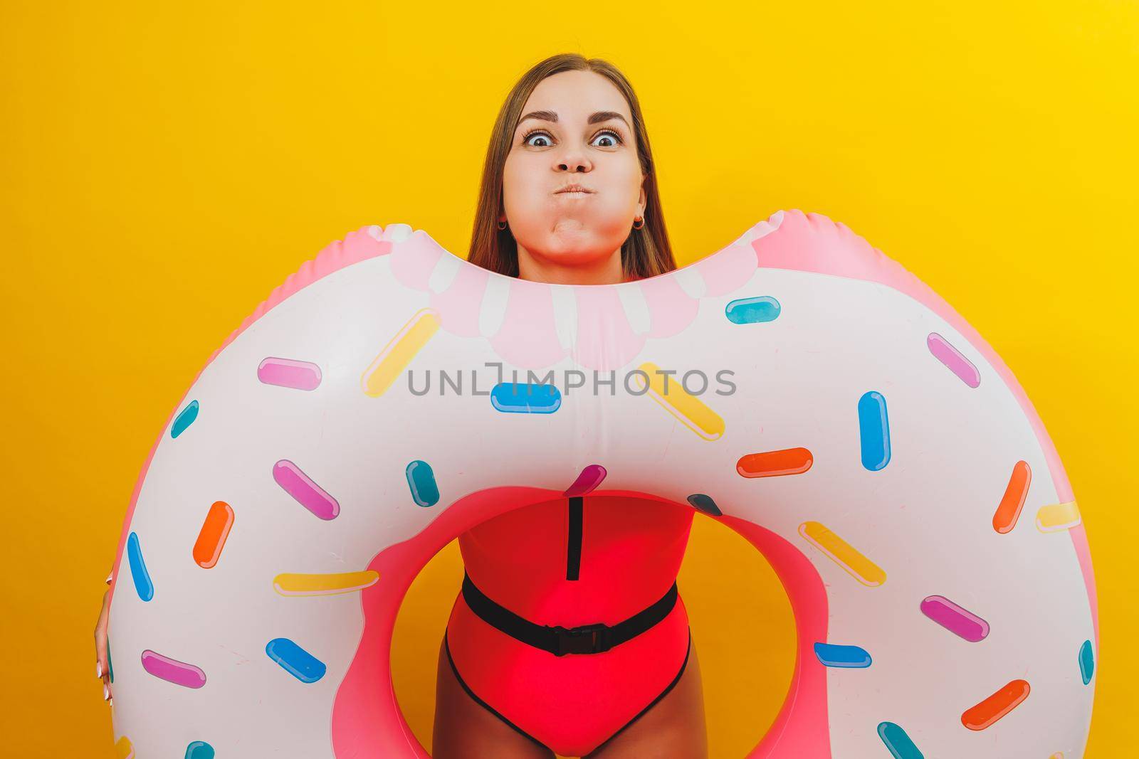 Emotional young woman wearing a pink swimsuit with an inflatable ring isolated on a bright yellow background. Summer hotel pool sea vacation sun tanning concept by Dmitrytph