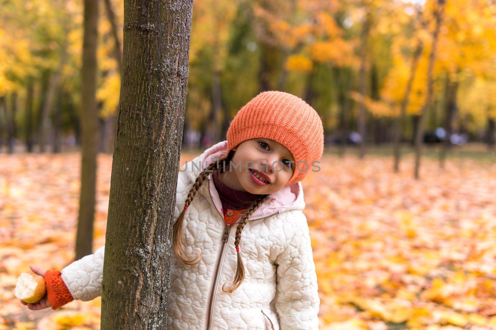 One happy funny child kid Girl orande Hat walking in park forest enjoying autumn fall nature weather. siblings Kid Collect falling leaves in baskets, playing hiding tree play hide and seek together.