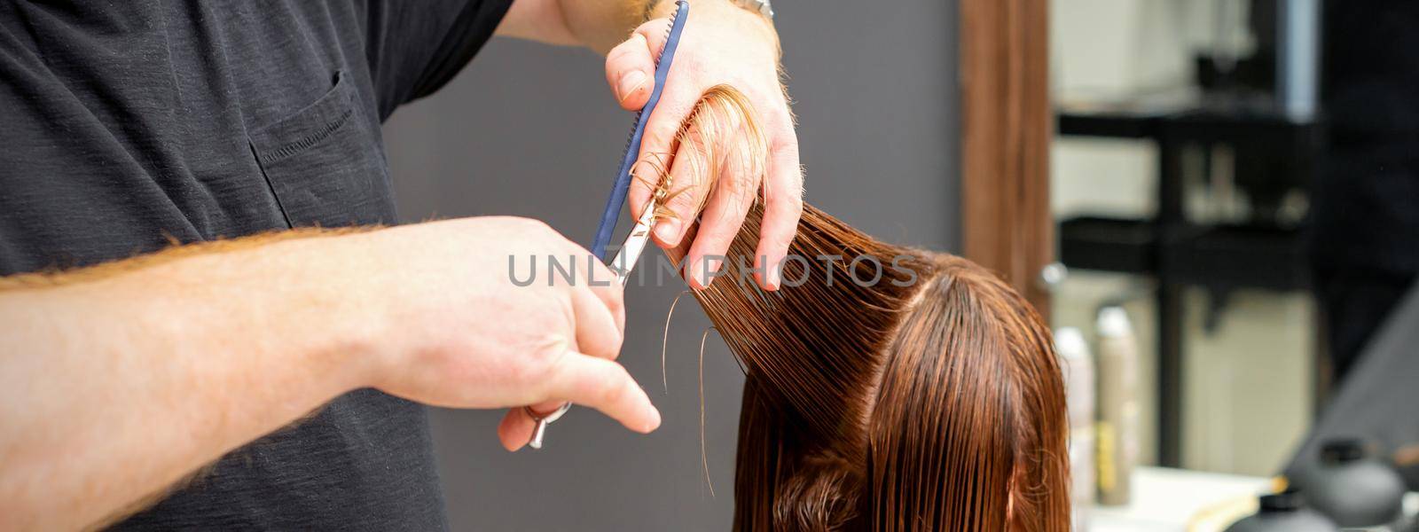 Woman having a new haircut. Male hairstylist cutting brown hair with scissors in a hair salon