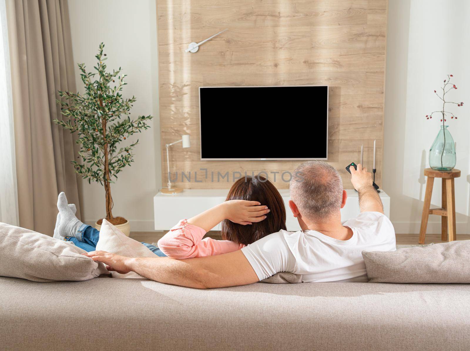 white man and woman in front of the TV lie on the sofa in the living room.