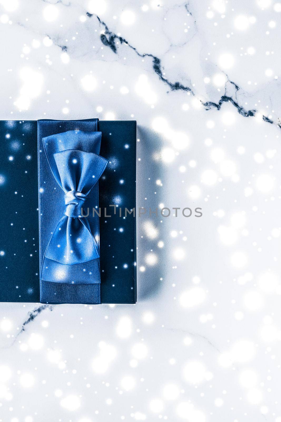 Winter holiday gift box with blue silk bow, snow glitter on marble background as Christmas and New Years presents for luxury beauty brand, flatlay design by Anneleven