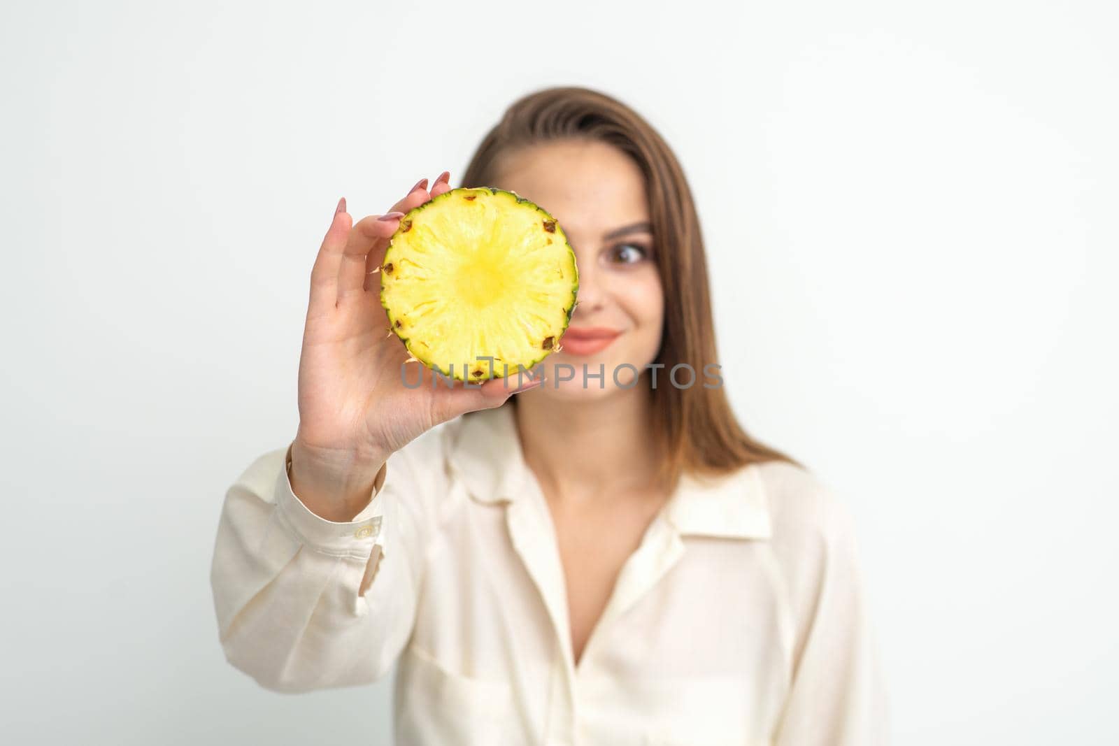 A young attractive pretty nice caucasian smiling woman holds ring slice pineapple covering her eye against a white background. Healthy eating concept