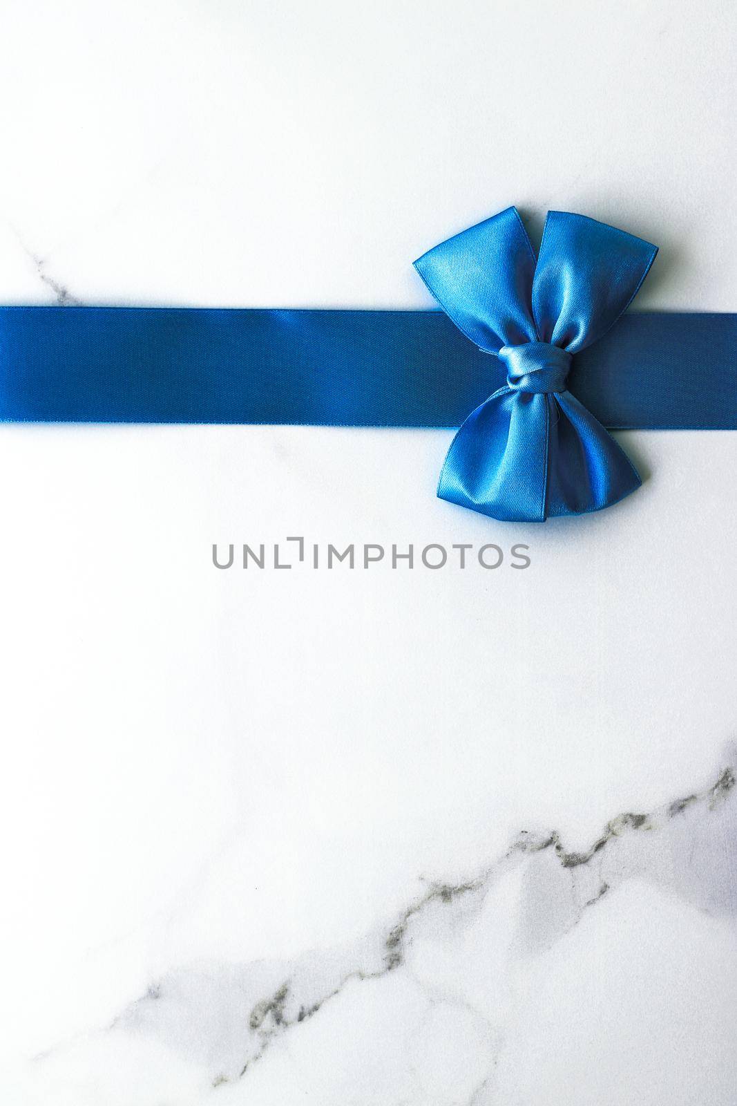 Happy holidays, festive decoration and brand sale promotion concept - Blue silk ribbon and bow on luxury marble background, holiday flatlay backdrop