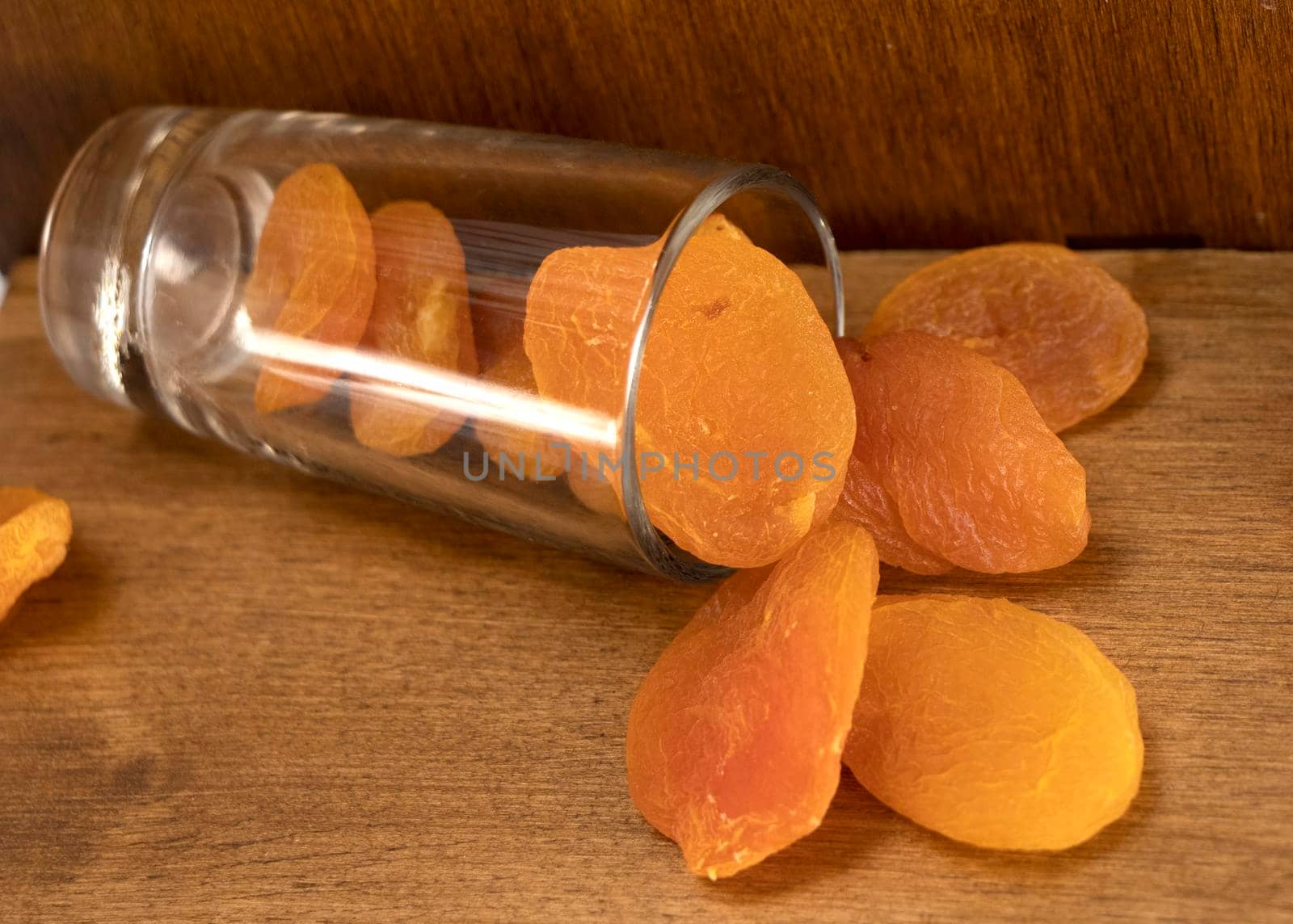 dried apricots are scattered from a glass on a wooden table. diet dessert. dried fruit orange. High quality photo