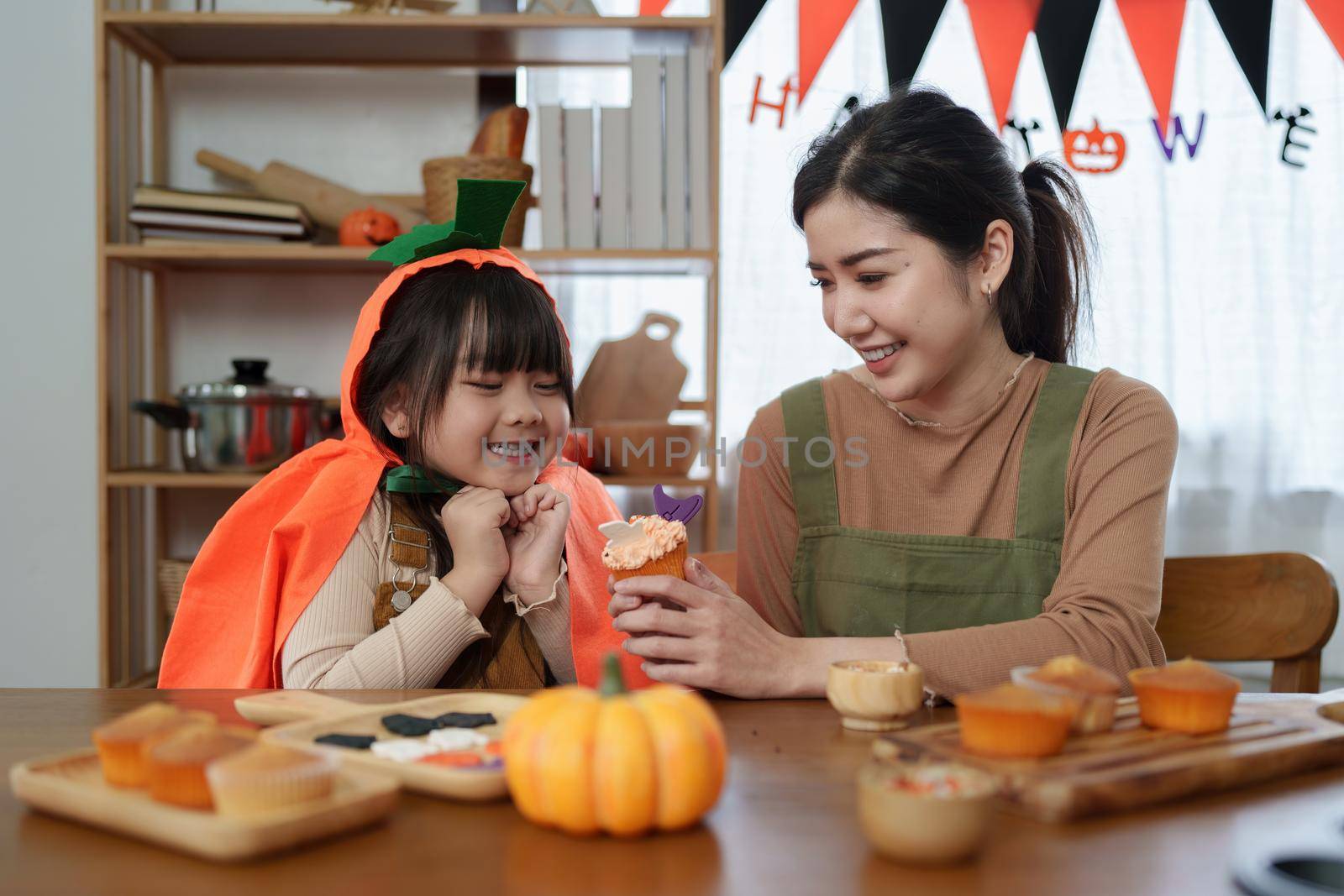 Young girl and mother at Halloween making treats and cupcake on table. Happy Halloween day by itchaznong