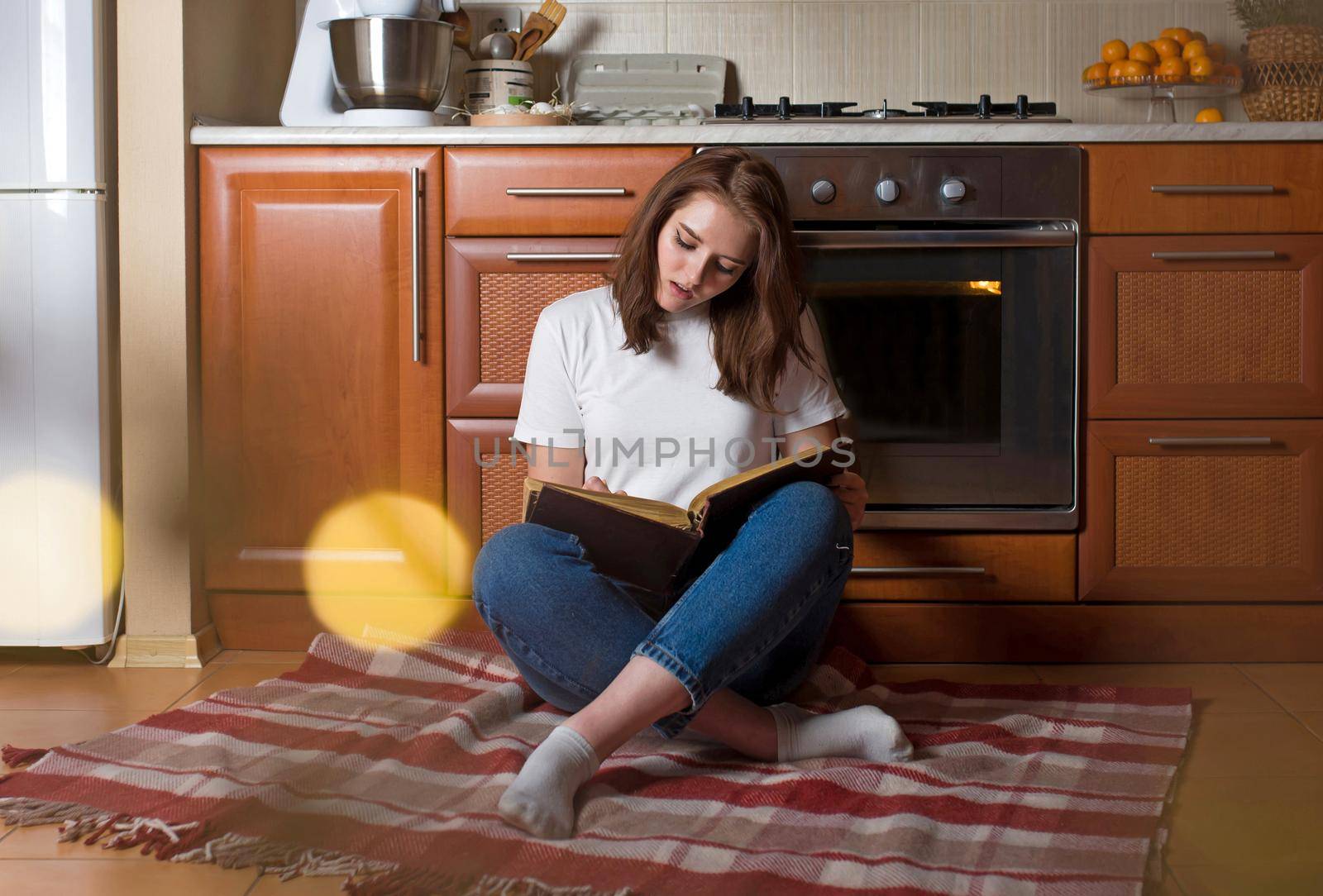 Young woman sitting on the kitchen floor, while relaxing at home. Healthy eating, food and lifestyle concept