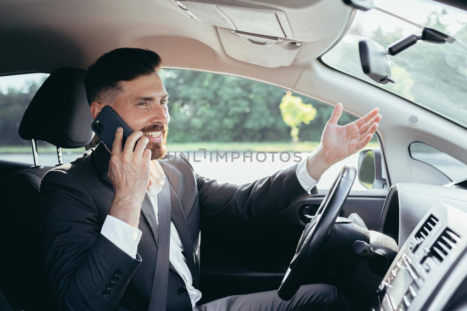 Young man with beard businessman driving a car in the parking lot smiling successful talking on the phone by voronaman
