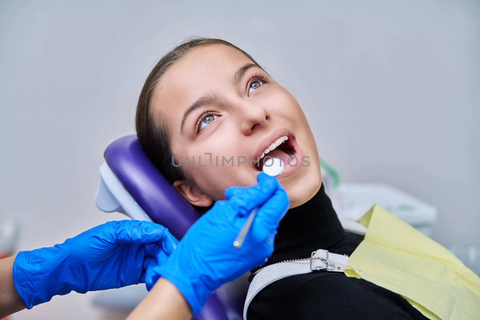 Young teenage female at dental checkup in clinic. Teenage girl sitting in chair, doctor dentist with tools examining patient's teeth. Adolescence, hygiene, dentistry, treatment, dental health care