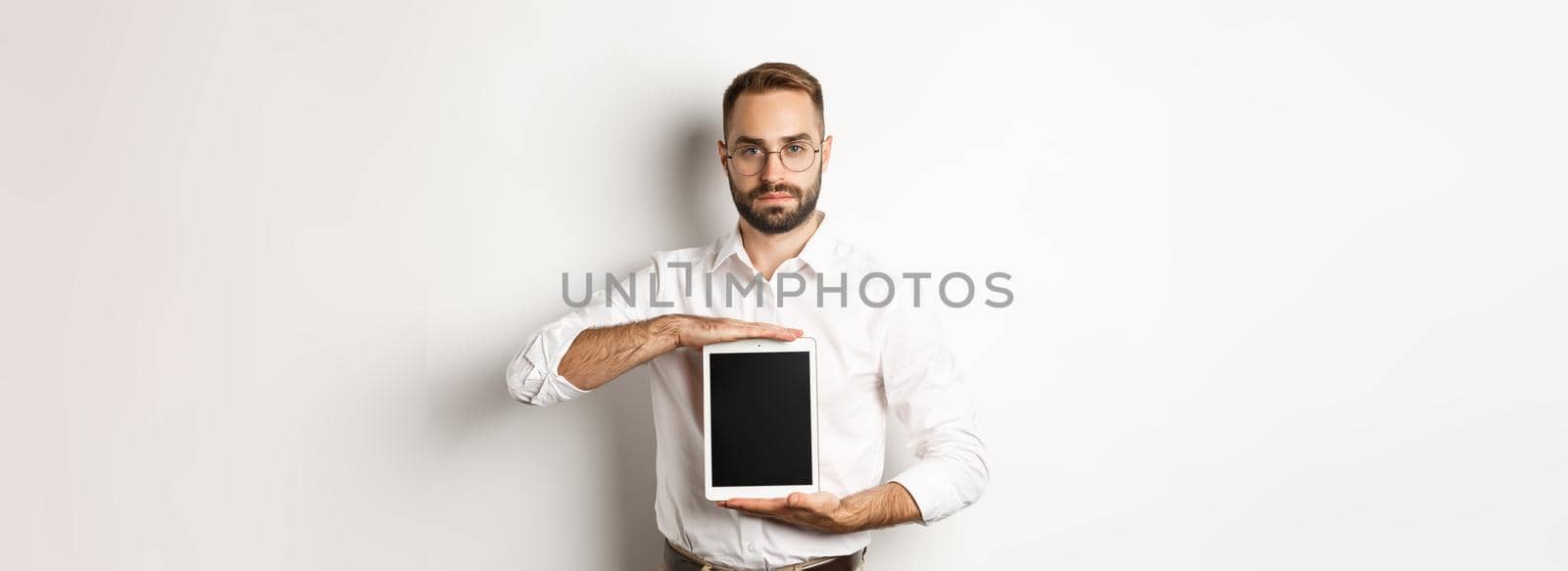 Confident bearded man showing digital tablet screen, demonstrating app, standing over white background.