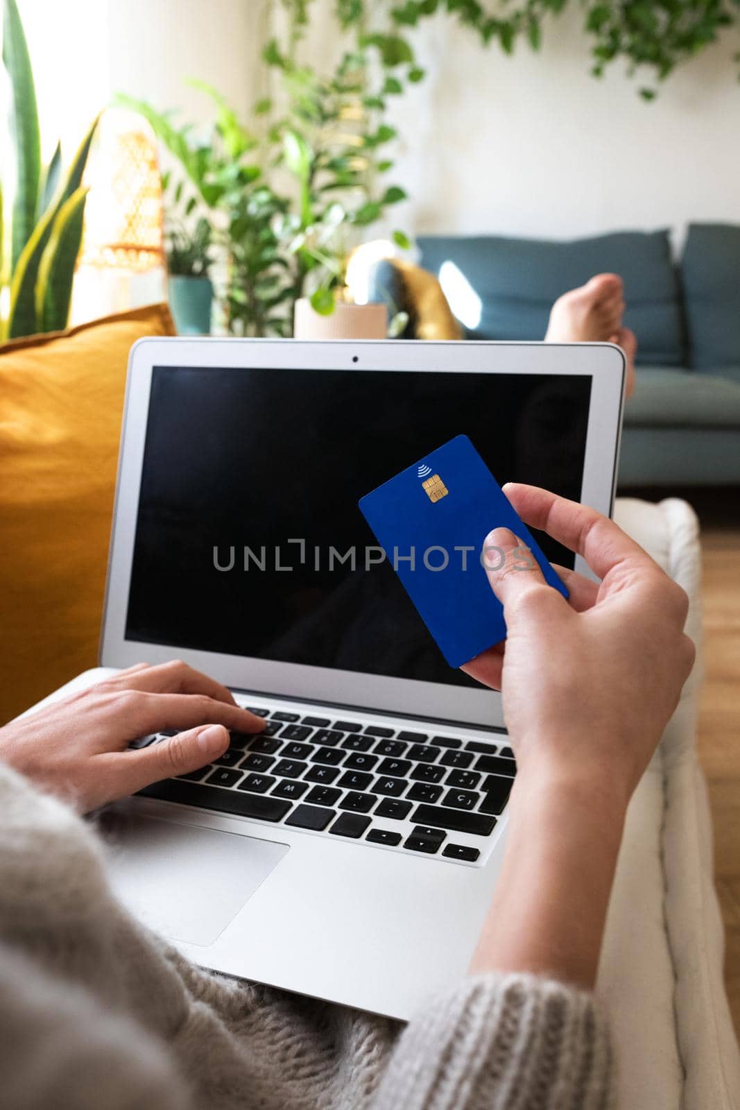 POV of young woman shopping online with credit card using laptop at home cozy living room. Copy space. Vertical image. E-commerce concept.