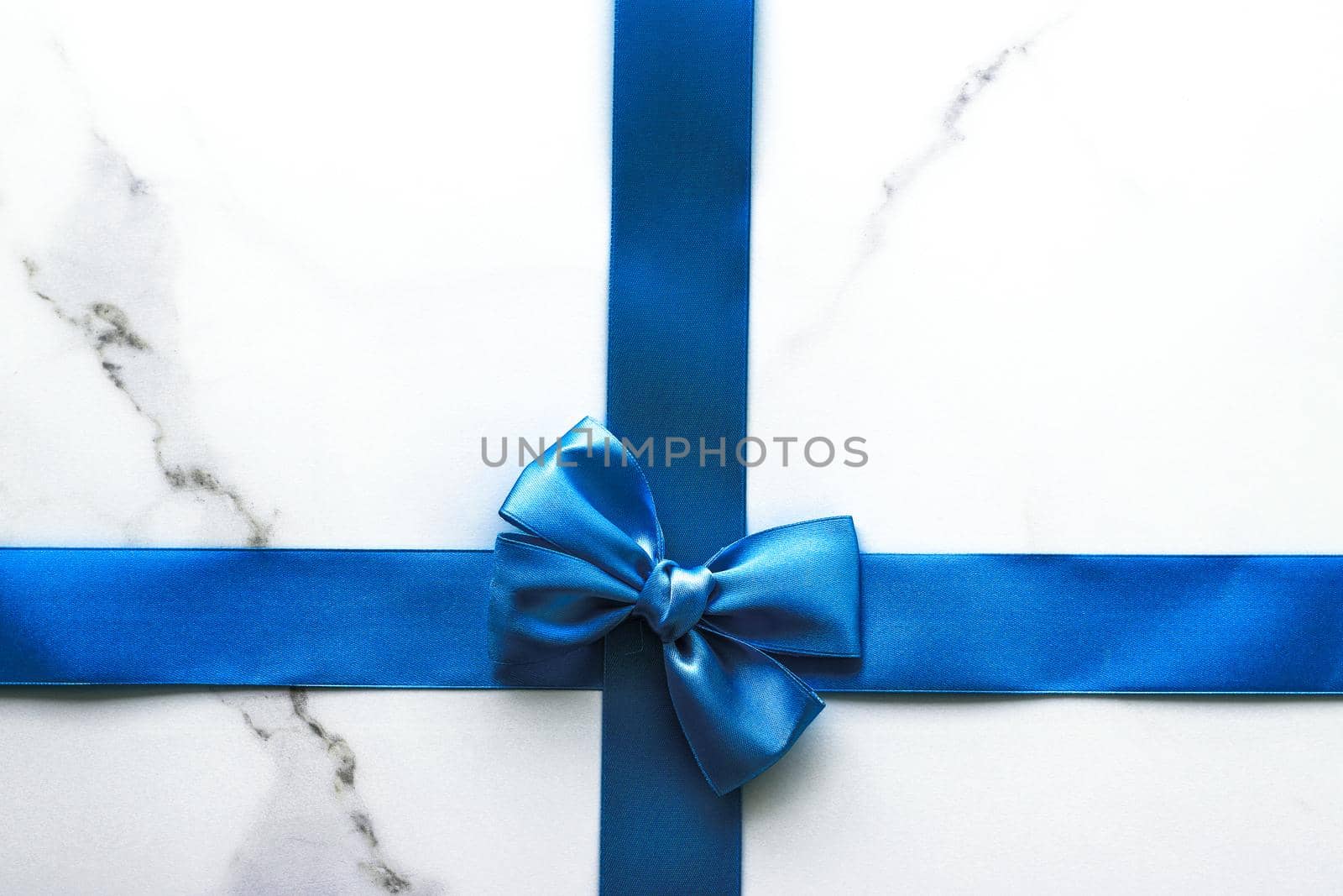 Happy holidays, festive decoration and brand sale promotion concept - Blue silk ribbon and bow on luxury marble background, holiday flatlay backdrop