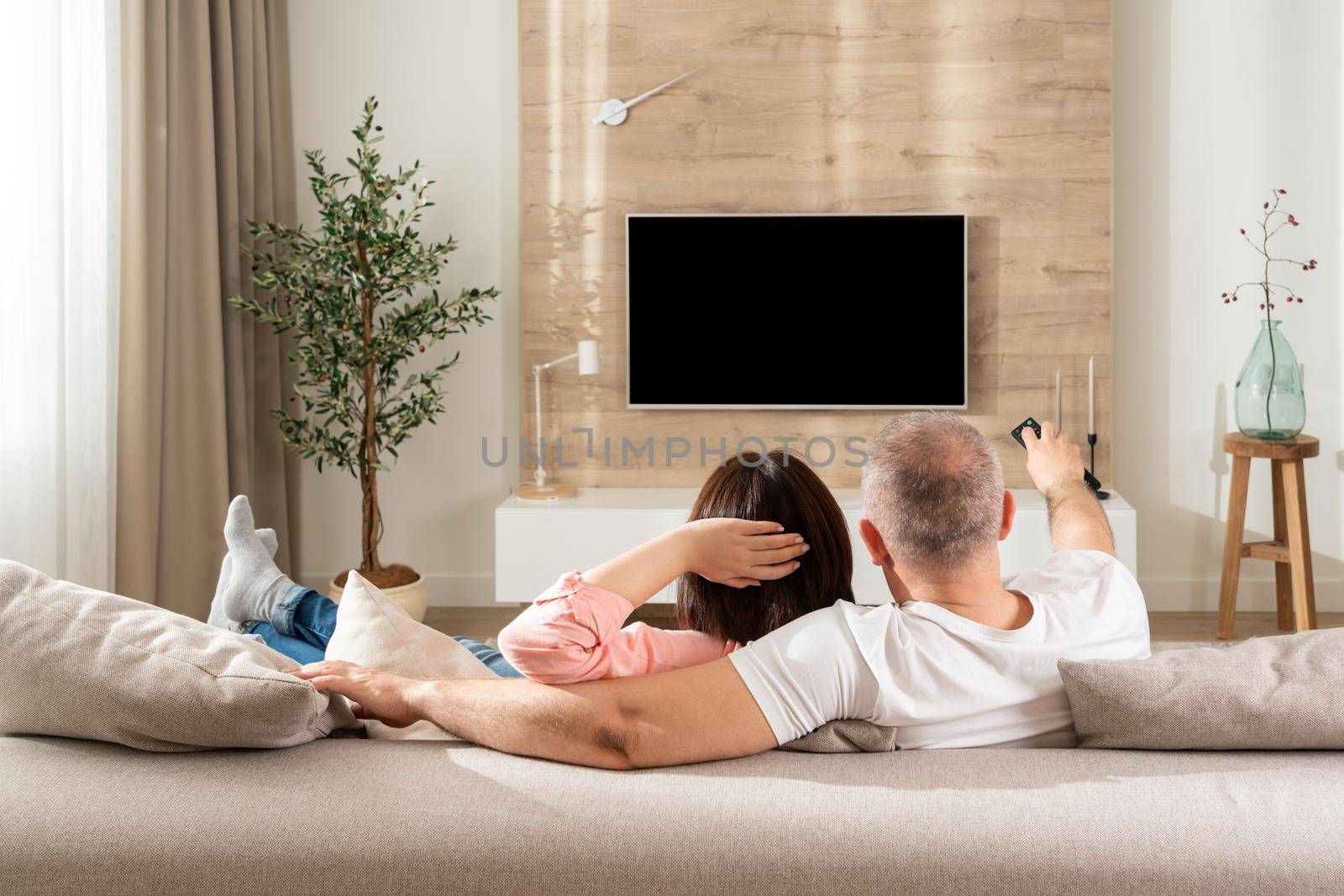 Cute family couple watching TV in modern living room.