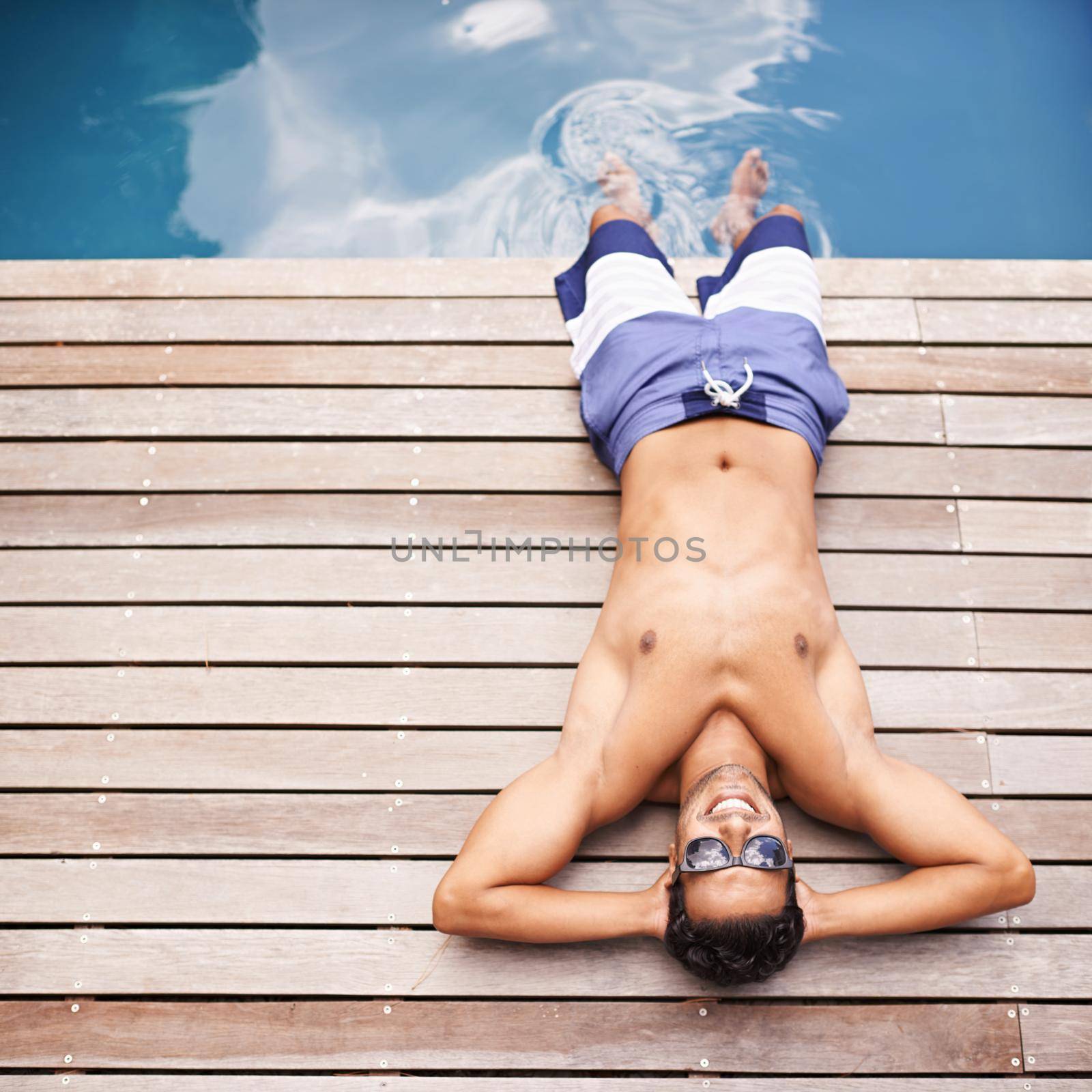 Taking it easy poolside. High angle shot of a young man lying by a pool. by YuriArcurs