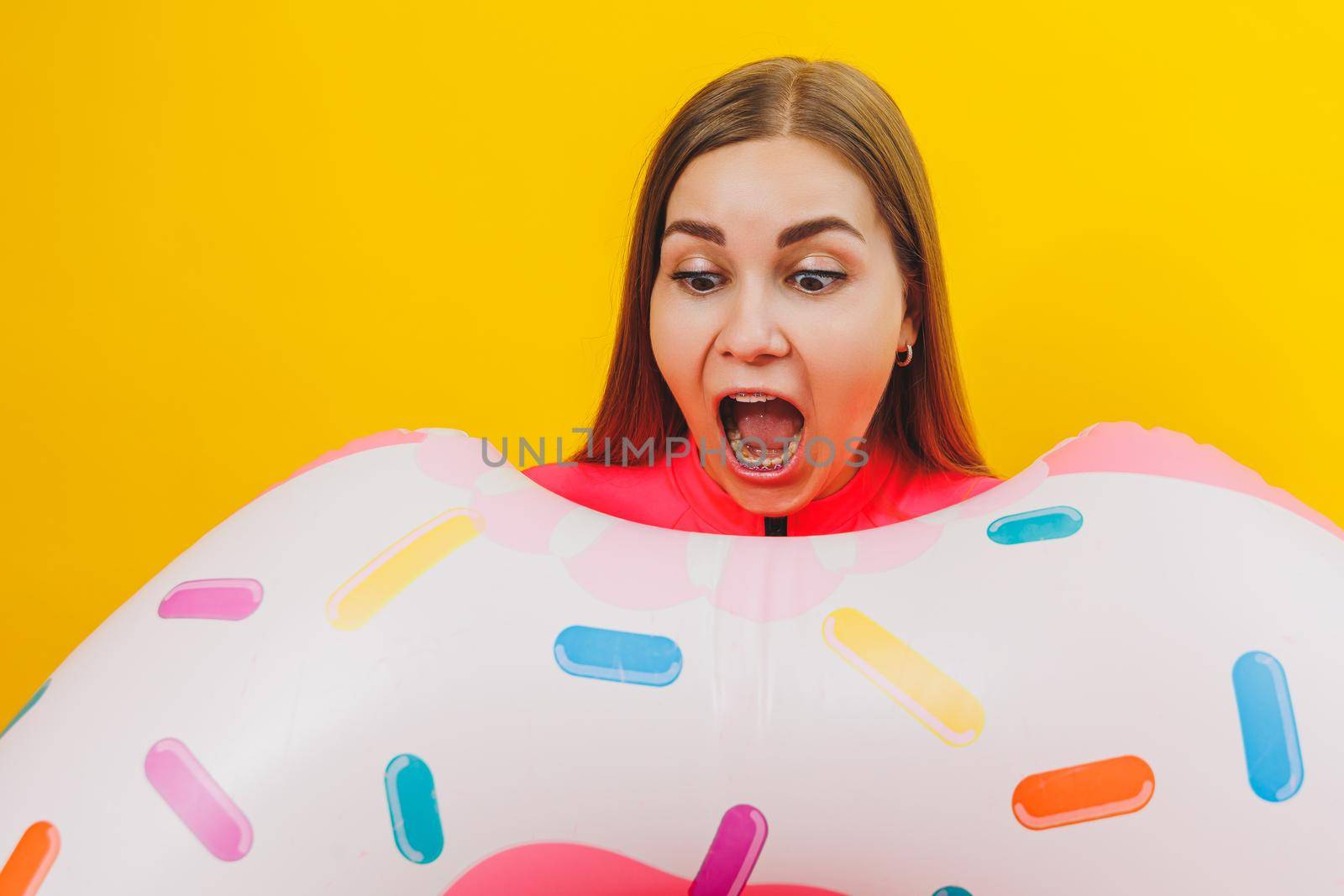 Emotional young woman wearing a pink swimsuit with an inflatable ring isolated on a bright yellow background. Summer hotel pool sea vacation sun tanning concept