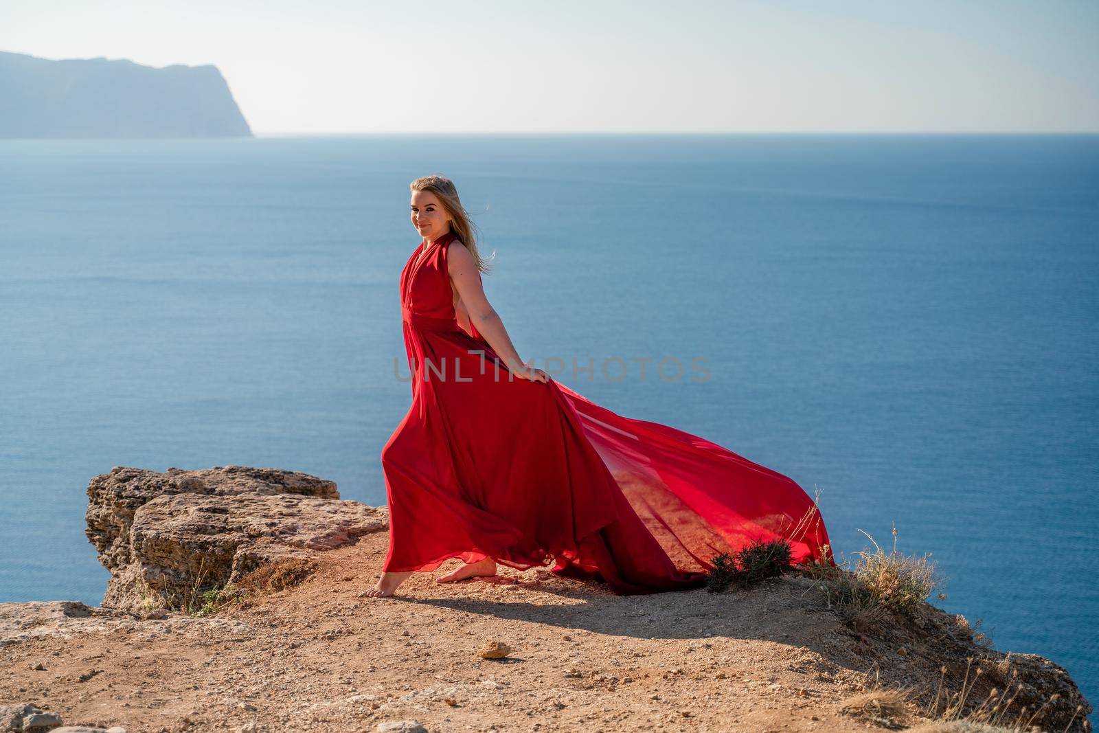 A woman in a red flying dress fluttering in the wind, against the backdrop of the sea