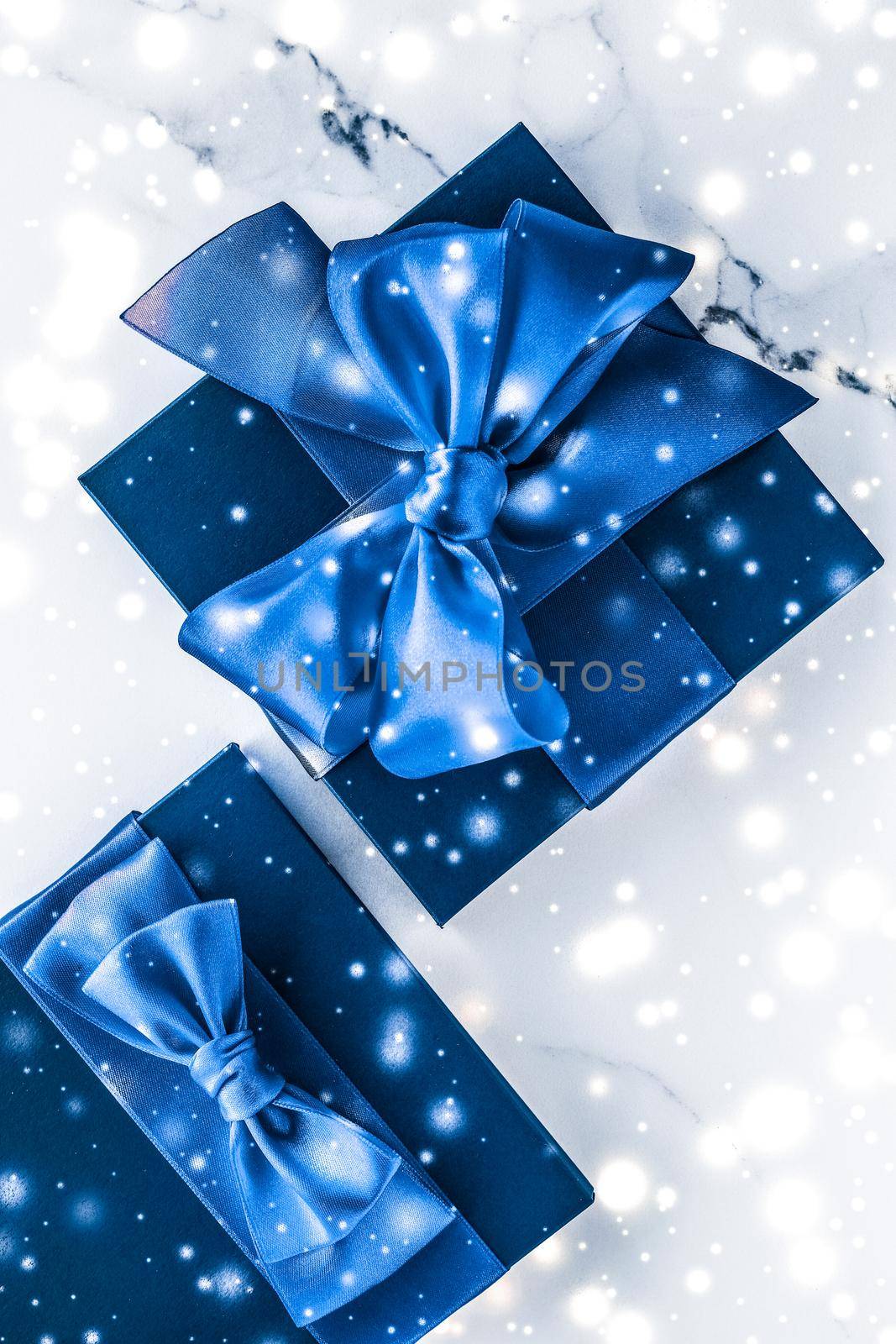 Branding, glamour and cold season concept - Winter holiday gift box with blue silk bow, snow glitter on marble background as Christmas and New Years presents for luxury beauty brand, flatlay design