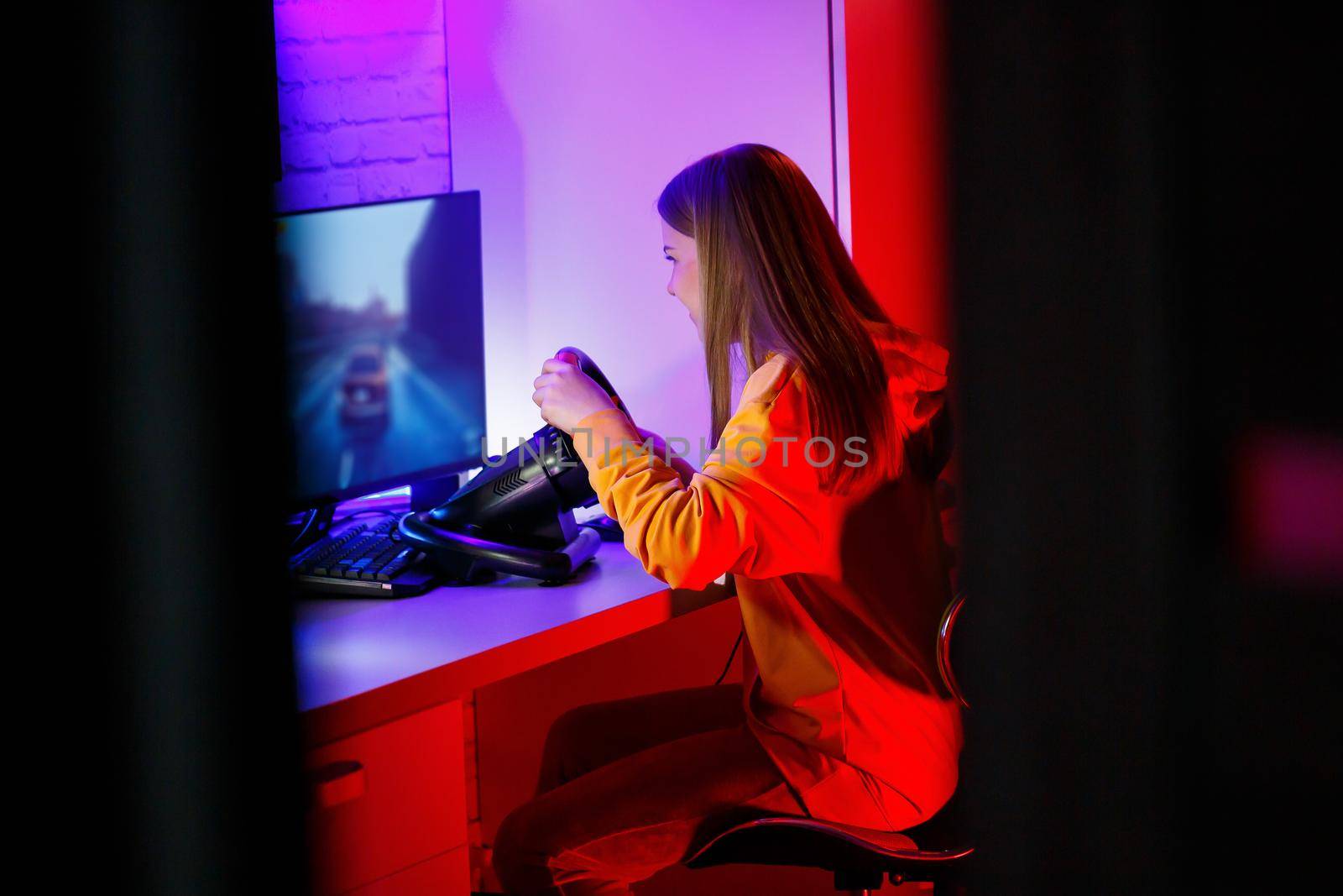 girl gamer playing racing on a computer. She uses a steering wheel. emotional play