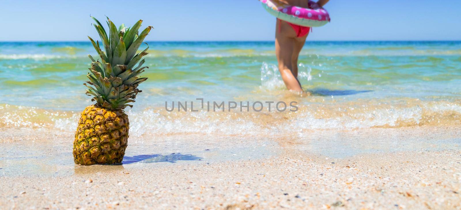 Pineapple on beach and kid running in the water background. Tropical background. Summer holiday concept. High quality photo