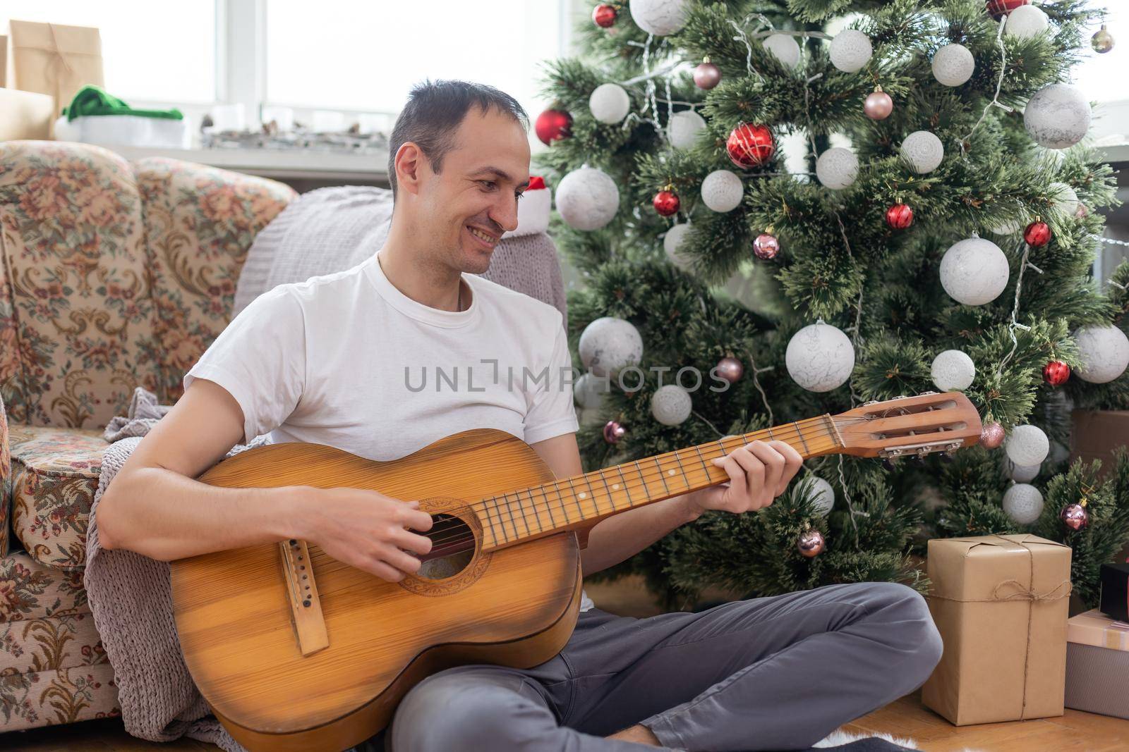 young handsome man sitting on the sofa, he is playing guitar, music, christmas, relax concept.