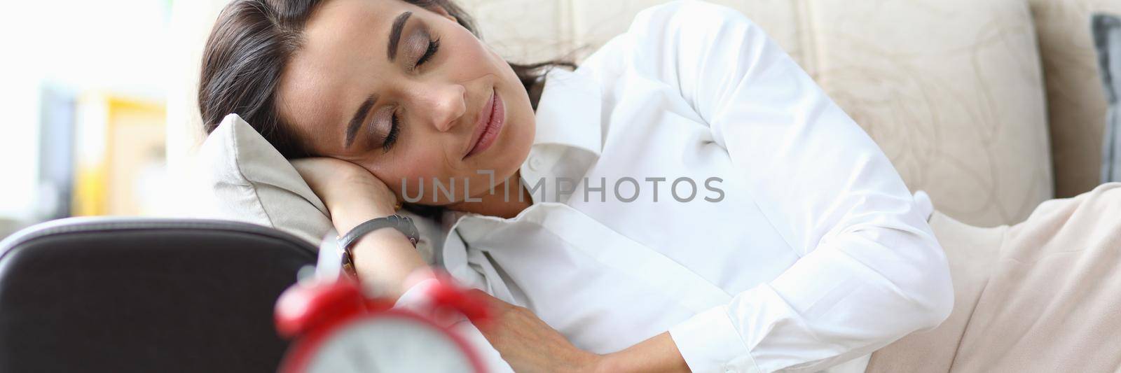 Young woman sleeps on sofa next to alarm clock by kuprevich