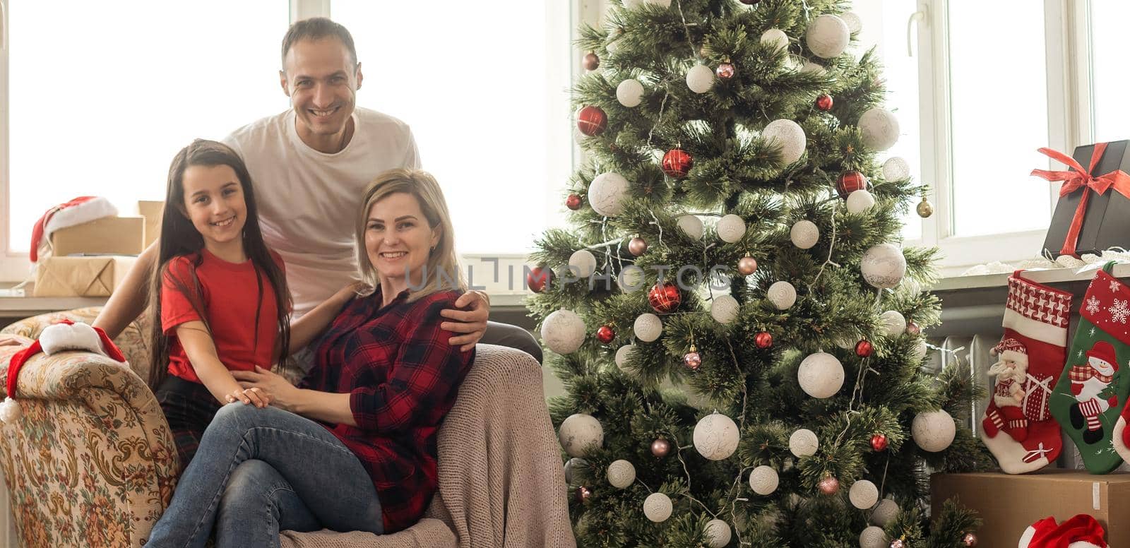 Happy family with cute daughter near Christmas tree together at home.