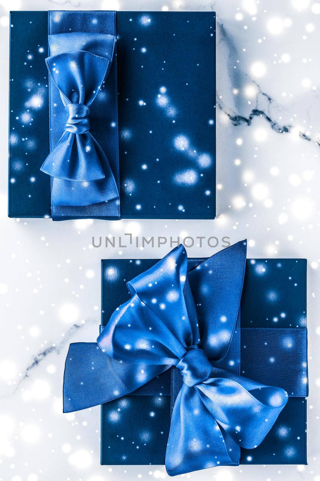 Branding, glamour and cold season concept - Winter holiday gift box with blue silk bow, snow glitter on marble background as Christmas and New Years presents for luxury beauty brand, flatlay design