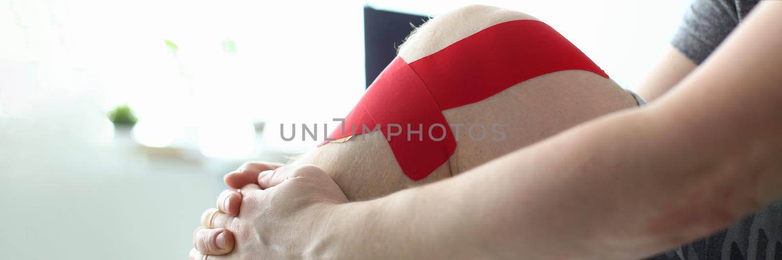 Therapeutic treatment of leg with red physio tape. Stretching knee joint concept