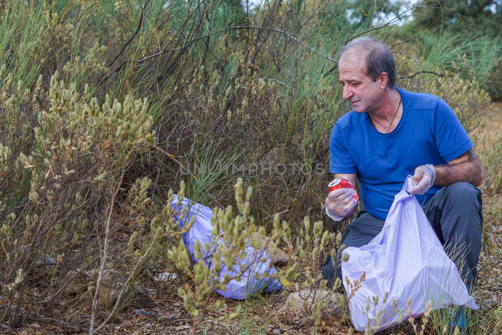 man with garbage bags and gloves cleaning the bush from polluting debris