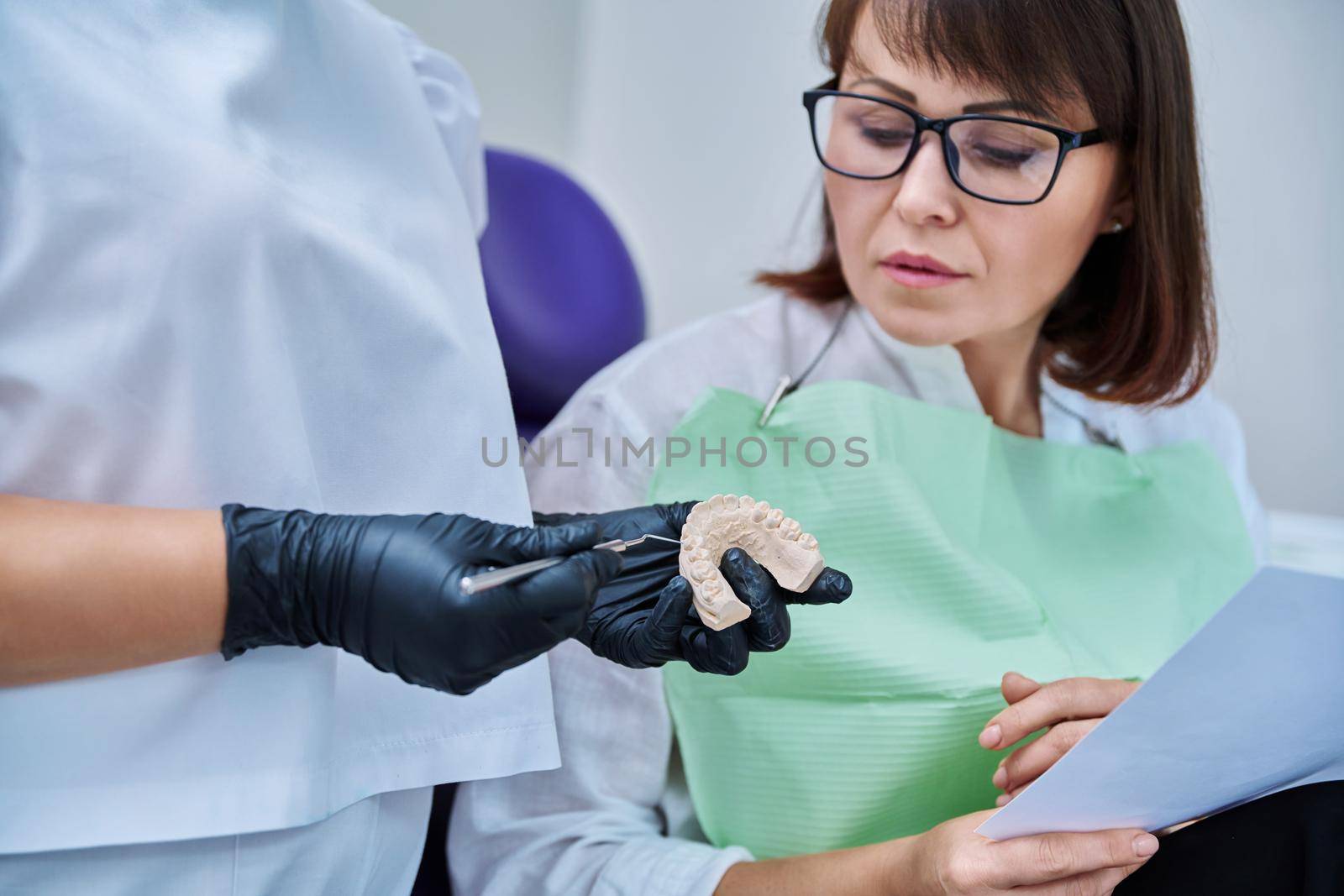 Plaster model of jaw in hands of doctor, female patient looking by VH-studio