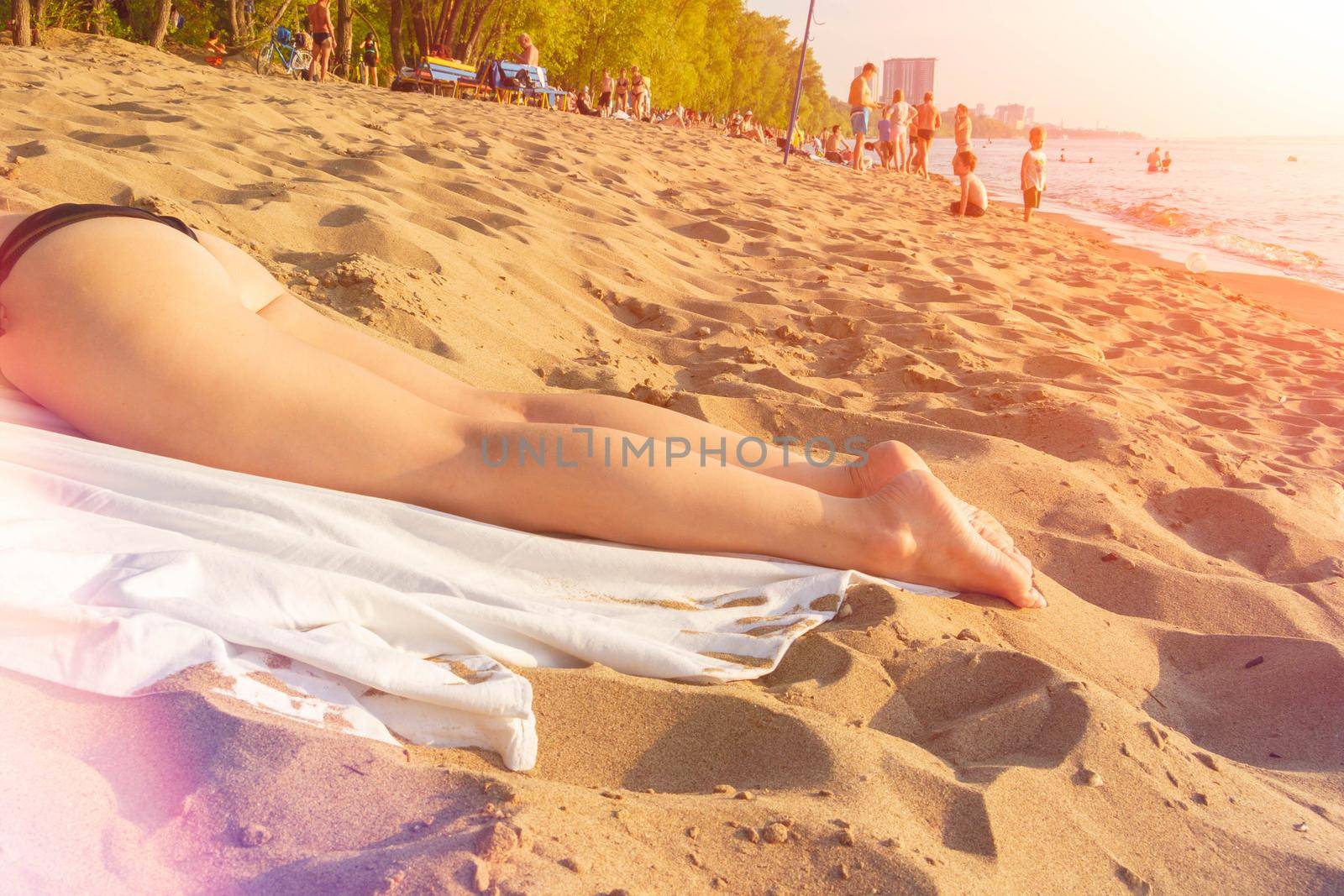 The girl is sunbathing on the sand. Legs of a young beautiful girl close-up. Tourists on the beach. Sunburn on the river. The sun shines brightly in summer.