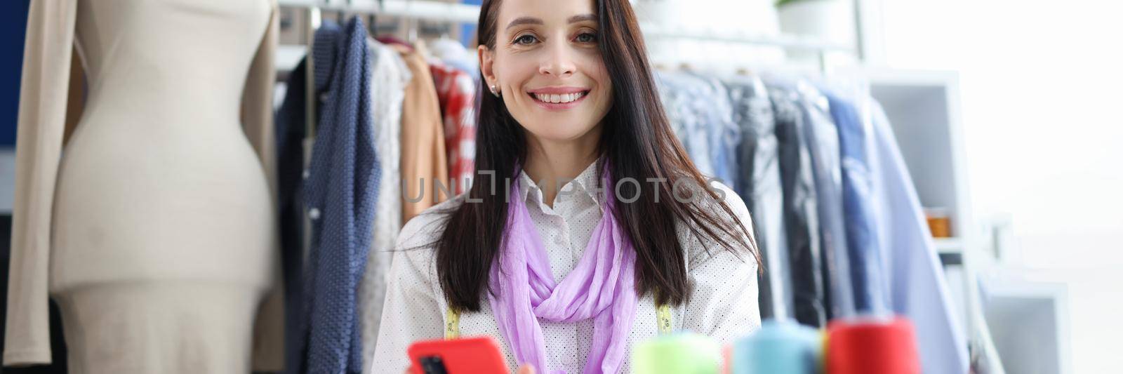 Smiling blooming woman holding smartphone at workplace. Profession fashion stylist concept