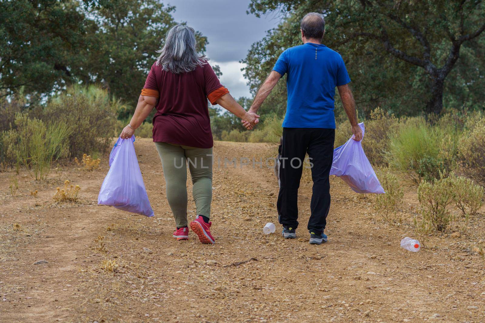 couple of environmentalists with garbage bags walking hand in hand by joseantona