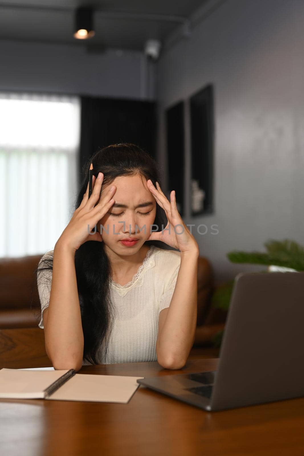 Tired asian female freelancer holding her head in hands, exhausted from overwork or stress at work by prathanchorruangsak