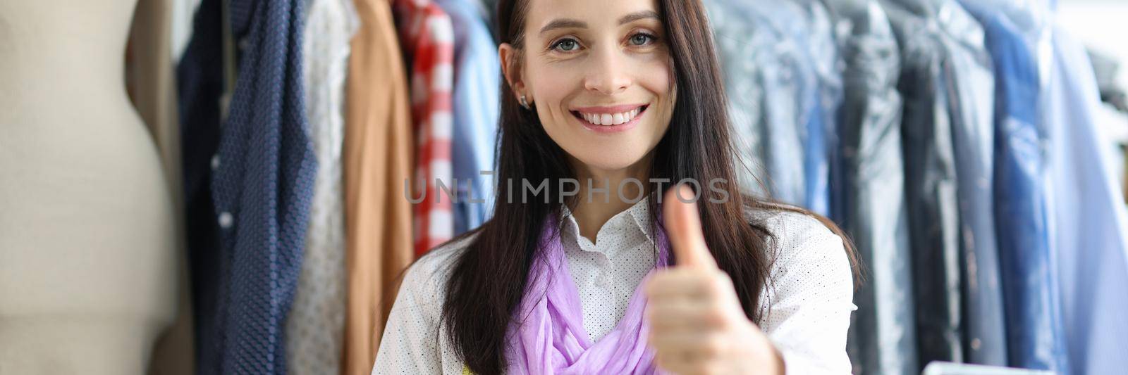 Young beautiful tailor woman showing thumbs up. Quality tailoring and clothing repair service concept