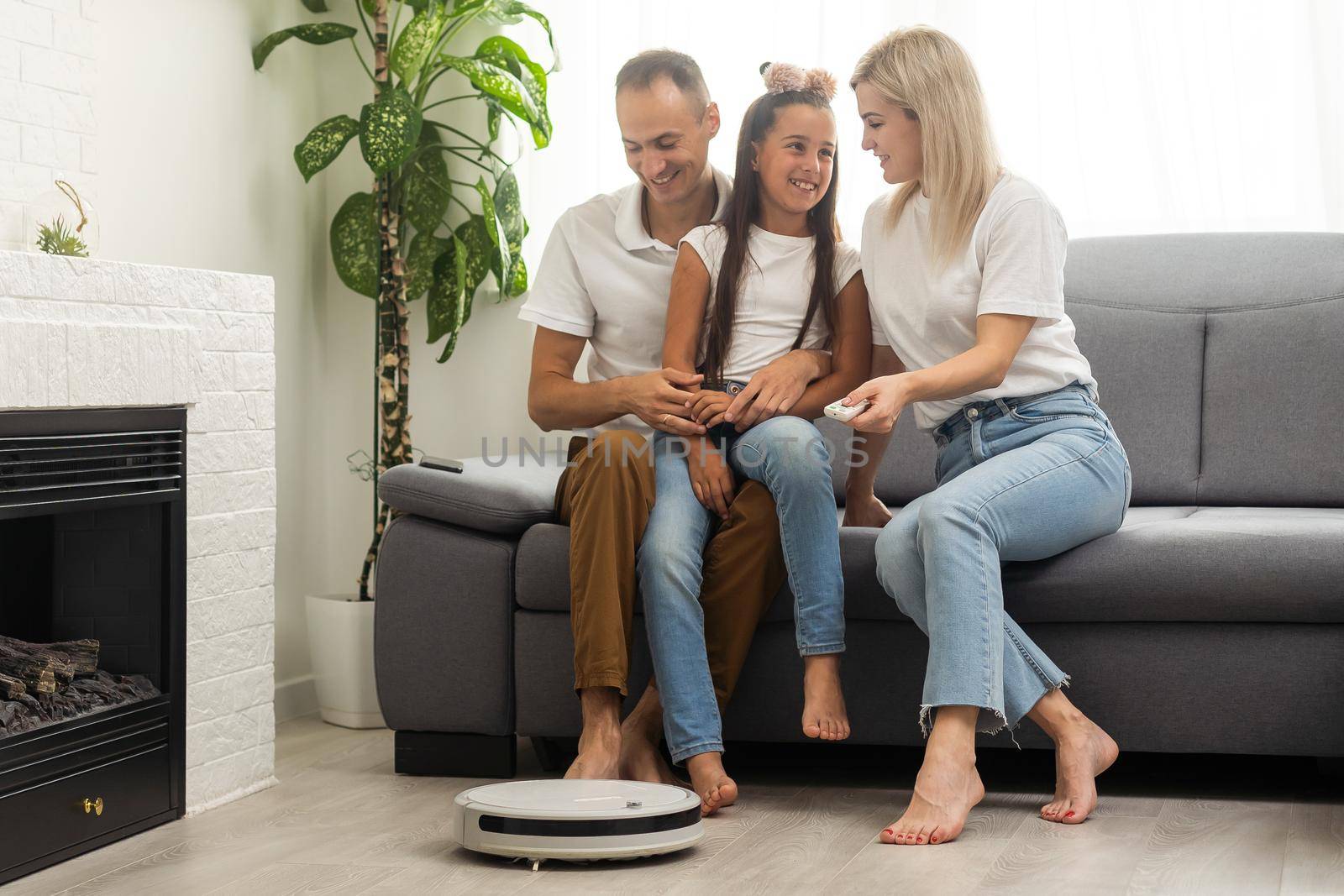 Young family resting on the couch while robotic vacuum cleaner doing its work at home. Household robots concept